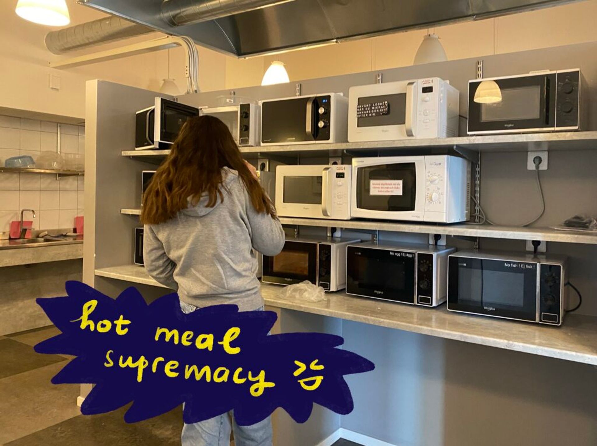 A person stands in front of a set of microwaves in a shared kitchen area.