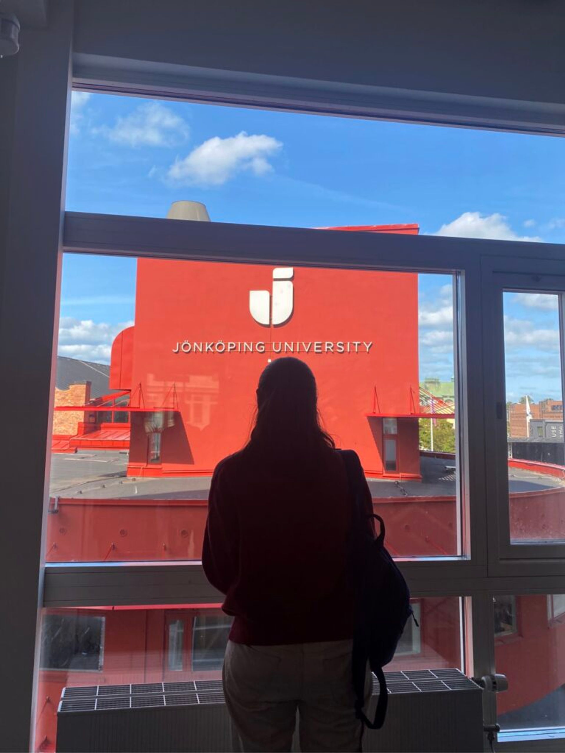 A person looks out a window at a Jönköping University sign.