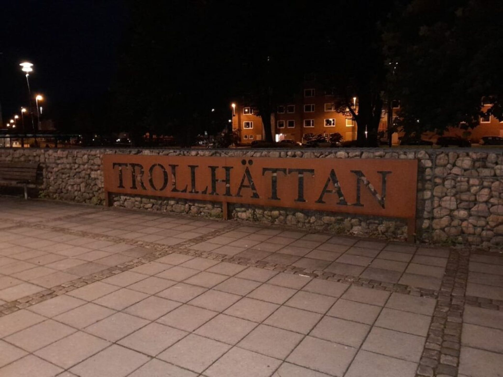 A sign indicating 'Trollhättan' positioned alongside a sidewalk.