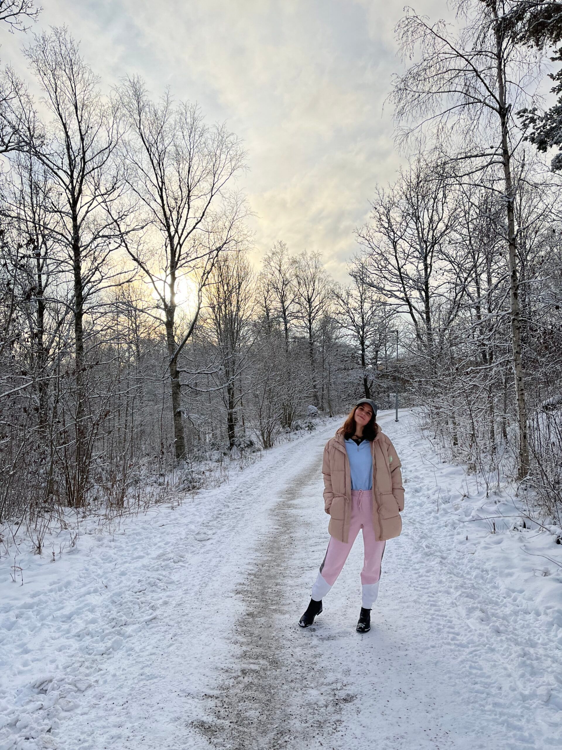 A woman standing on a snow-covered road lined with trees.