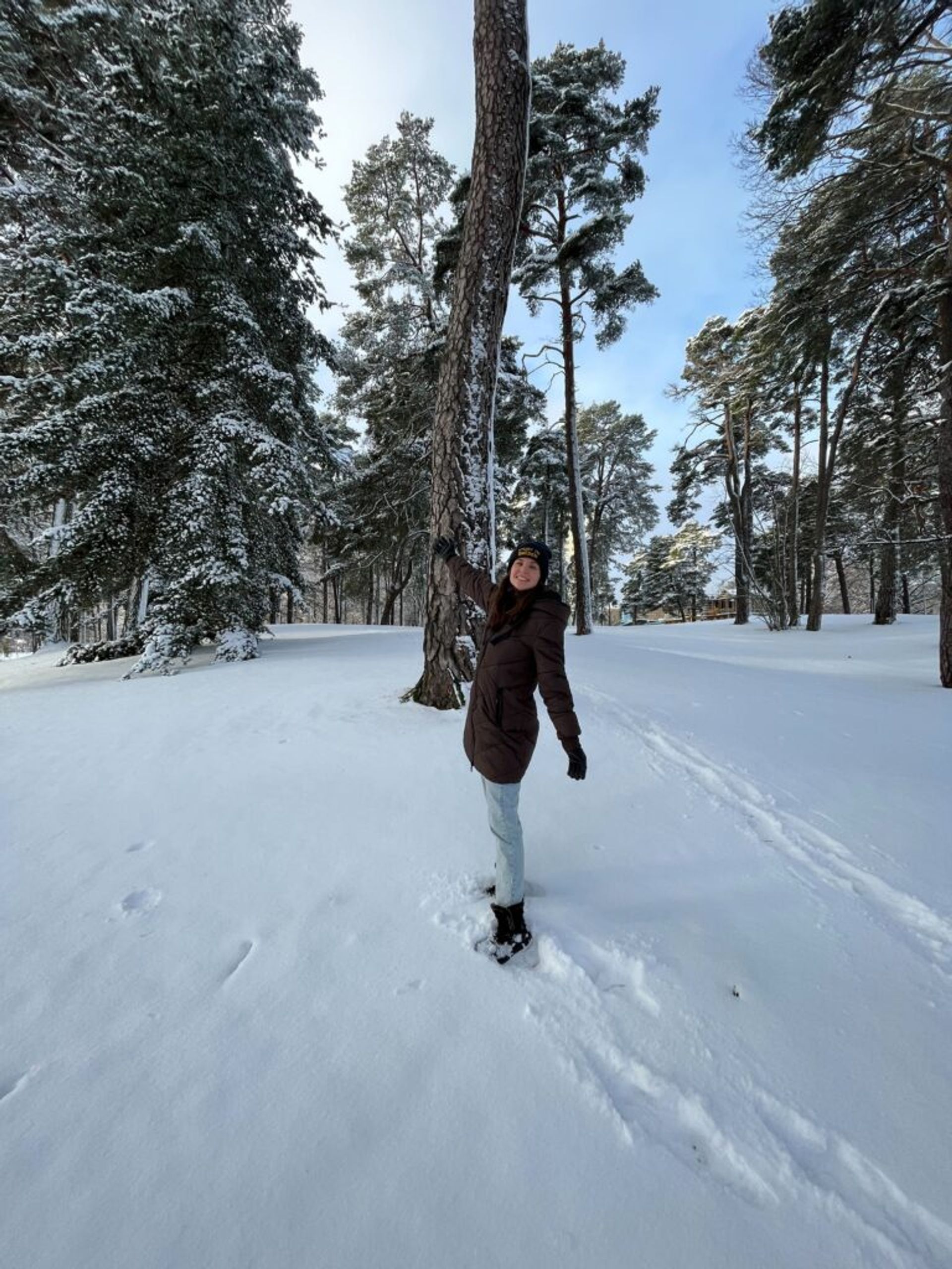 A woman in winter attire stands in a snow-covered forest.