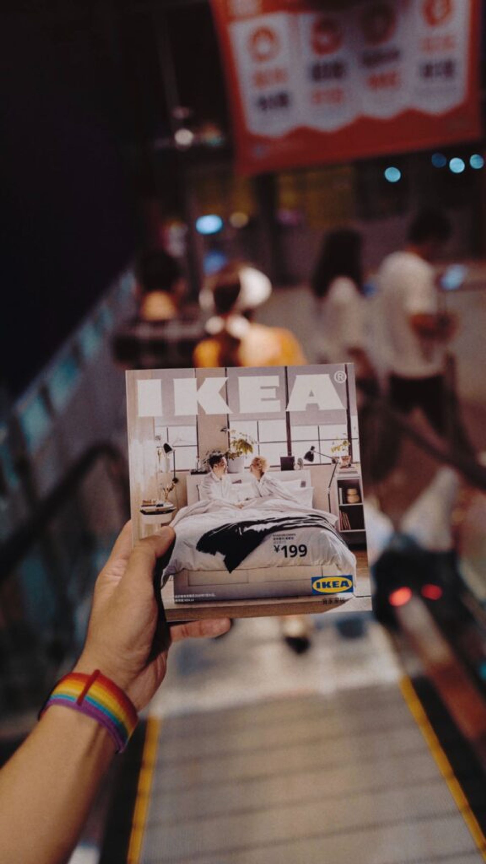 A close-up of a hand holding an IKEA brochure on an moving walkway.