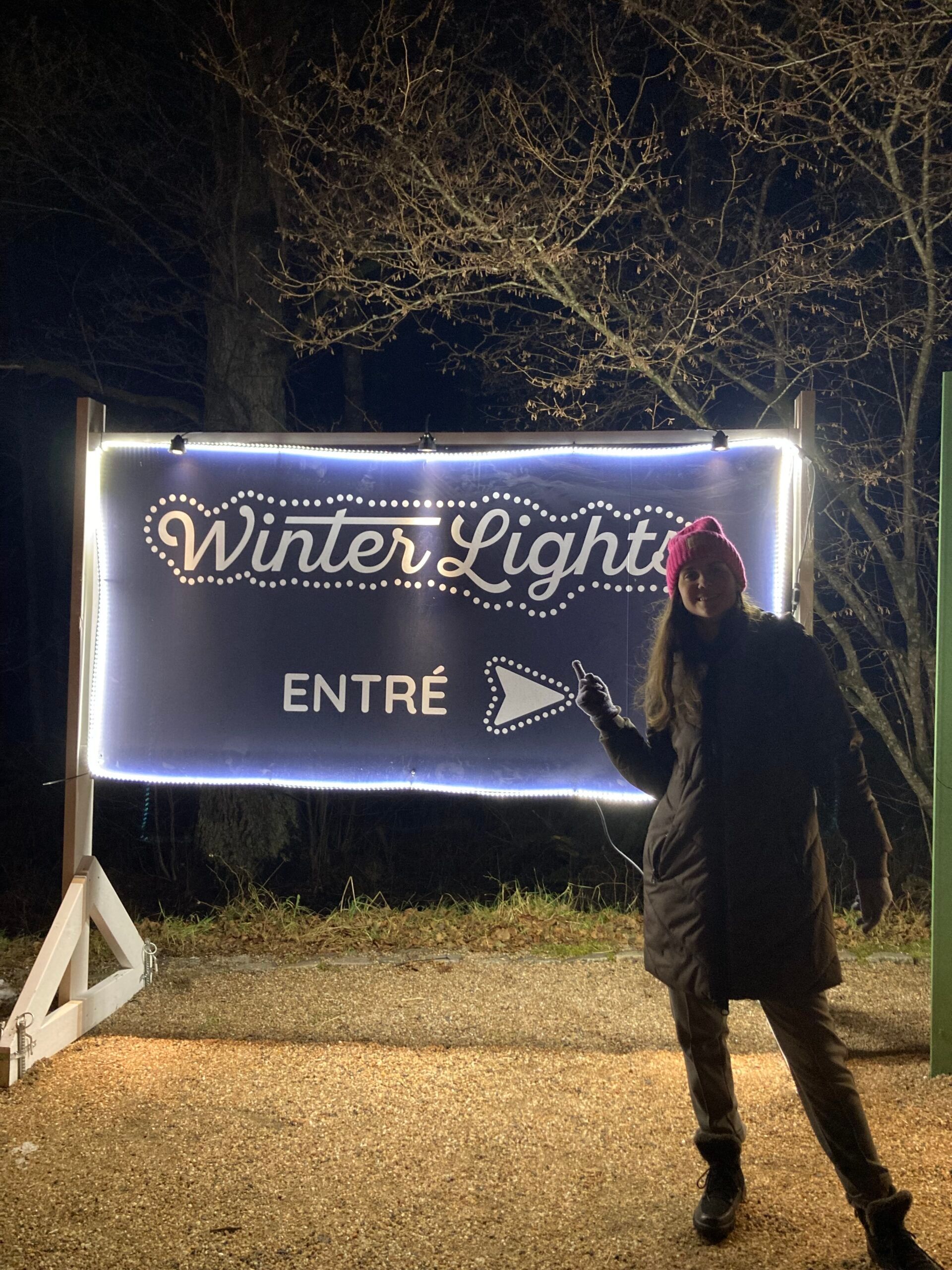 A woman in front of a sign pointing towards the entrance for the Winter Lights Exhibition.