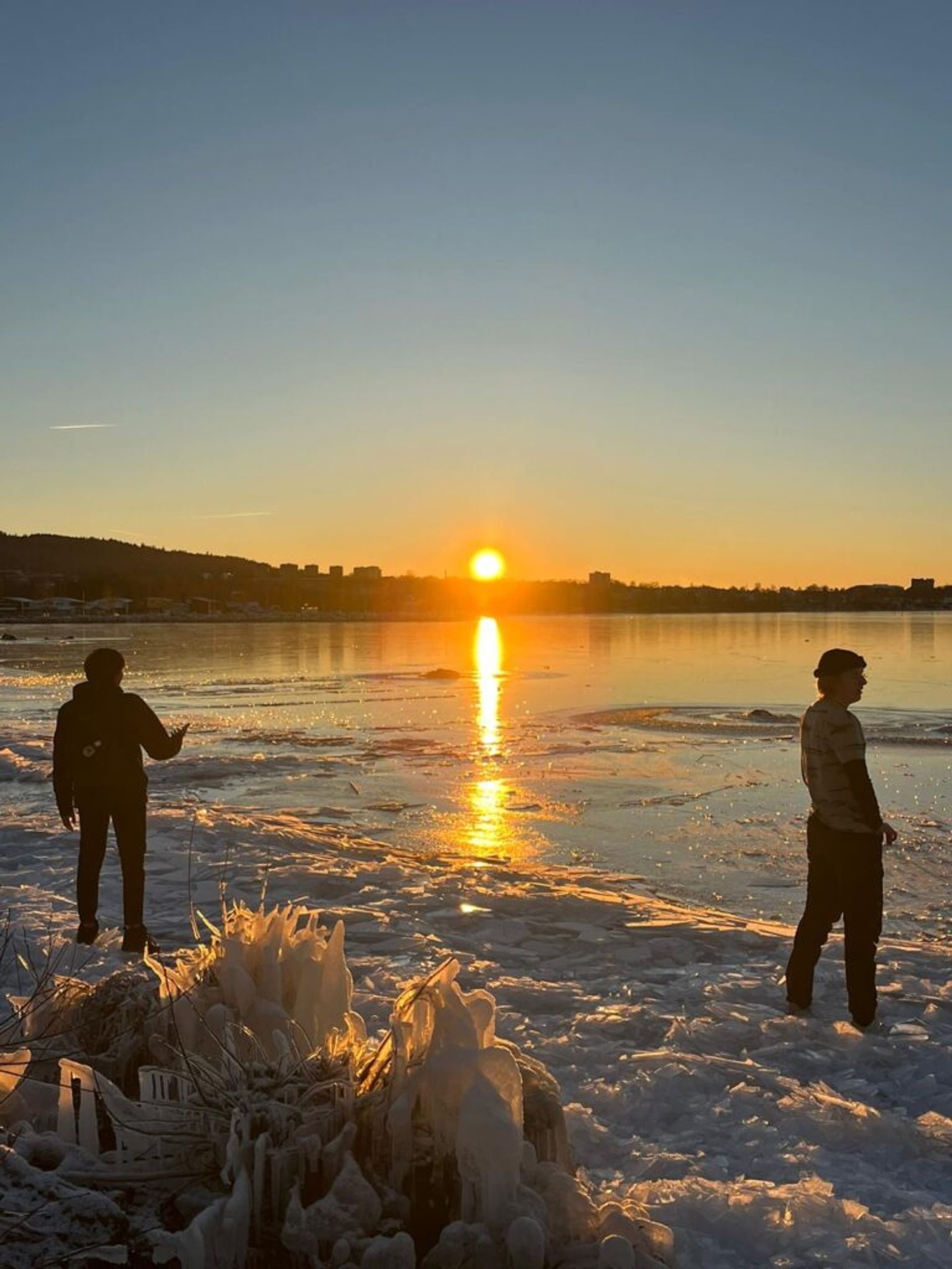 two students standing on a frozen lake watching sunset over Vättern in Jönköping