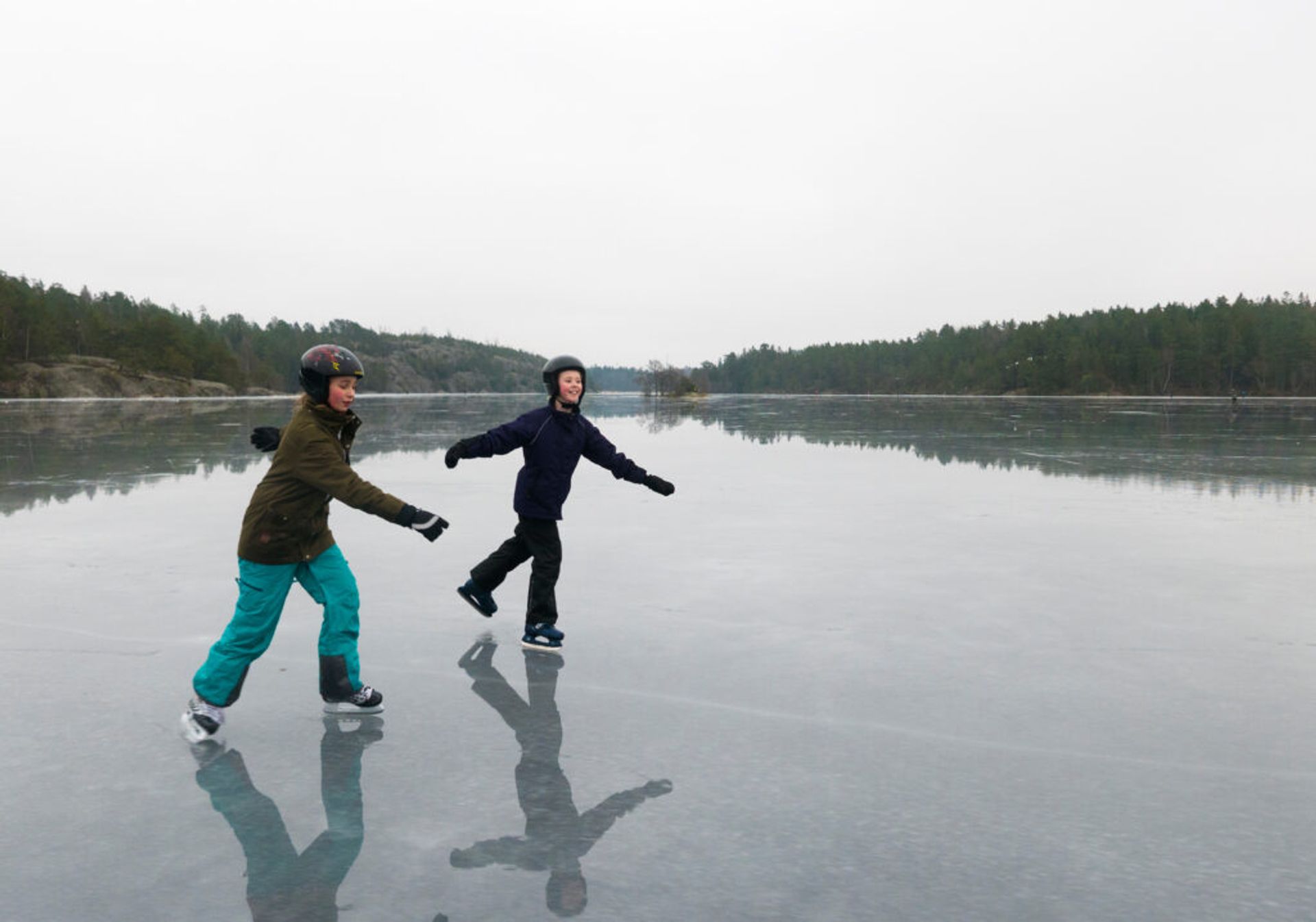 Two people ice skating on a frozen lake on a gloomy day.