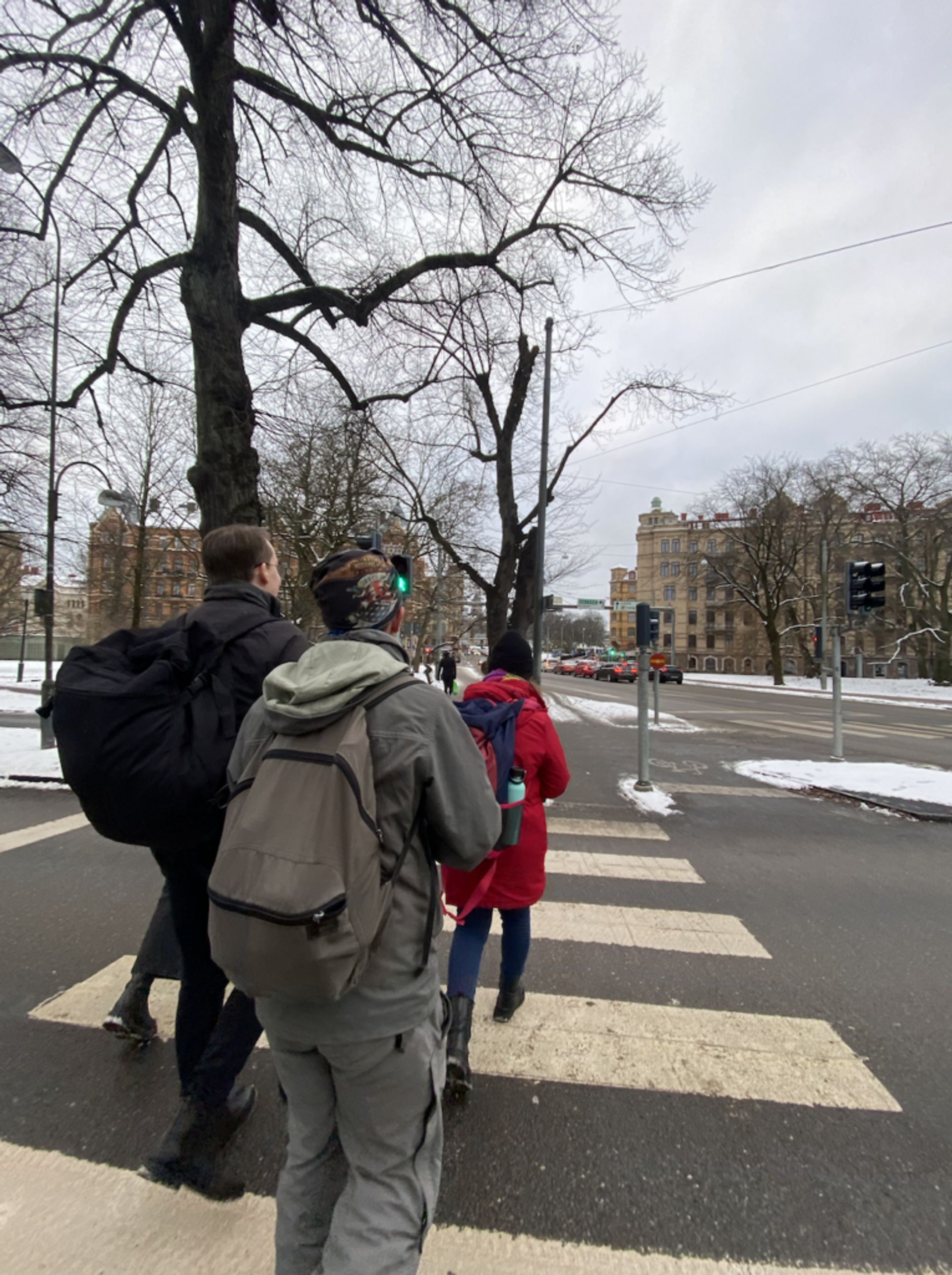 International students, dressed in winter attire, are crossing a zebra crossing in an urban environment on a cloudy day.