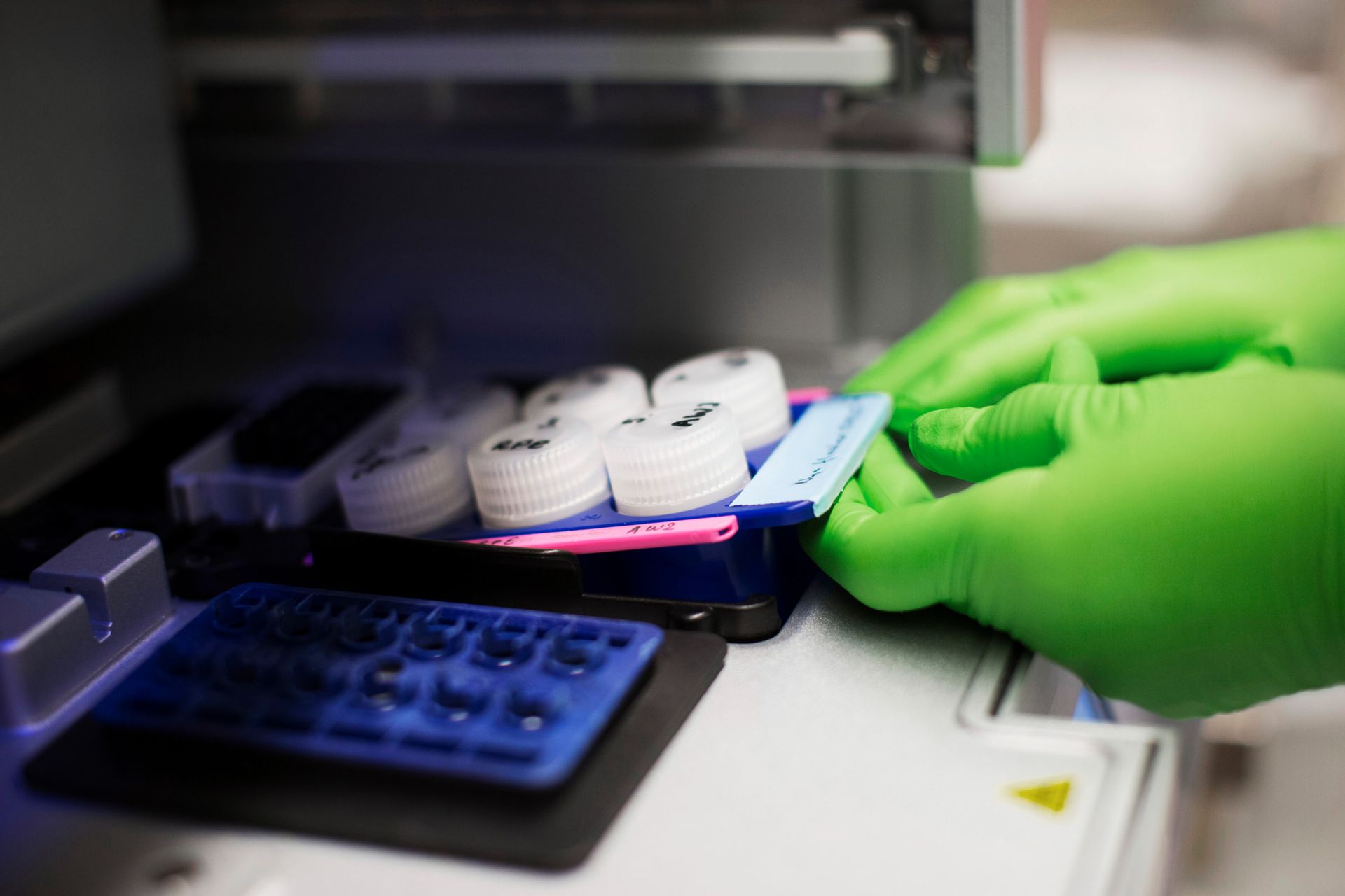 A close-up photo capturing a laboratory setting, where a person's hands, clad in bright green latex gloves, can be seen handling various laboratory items.