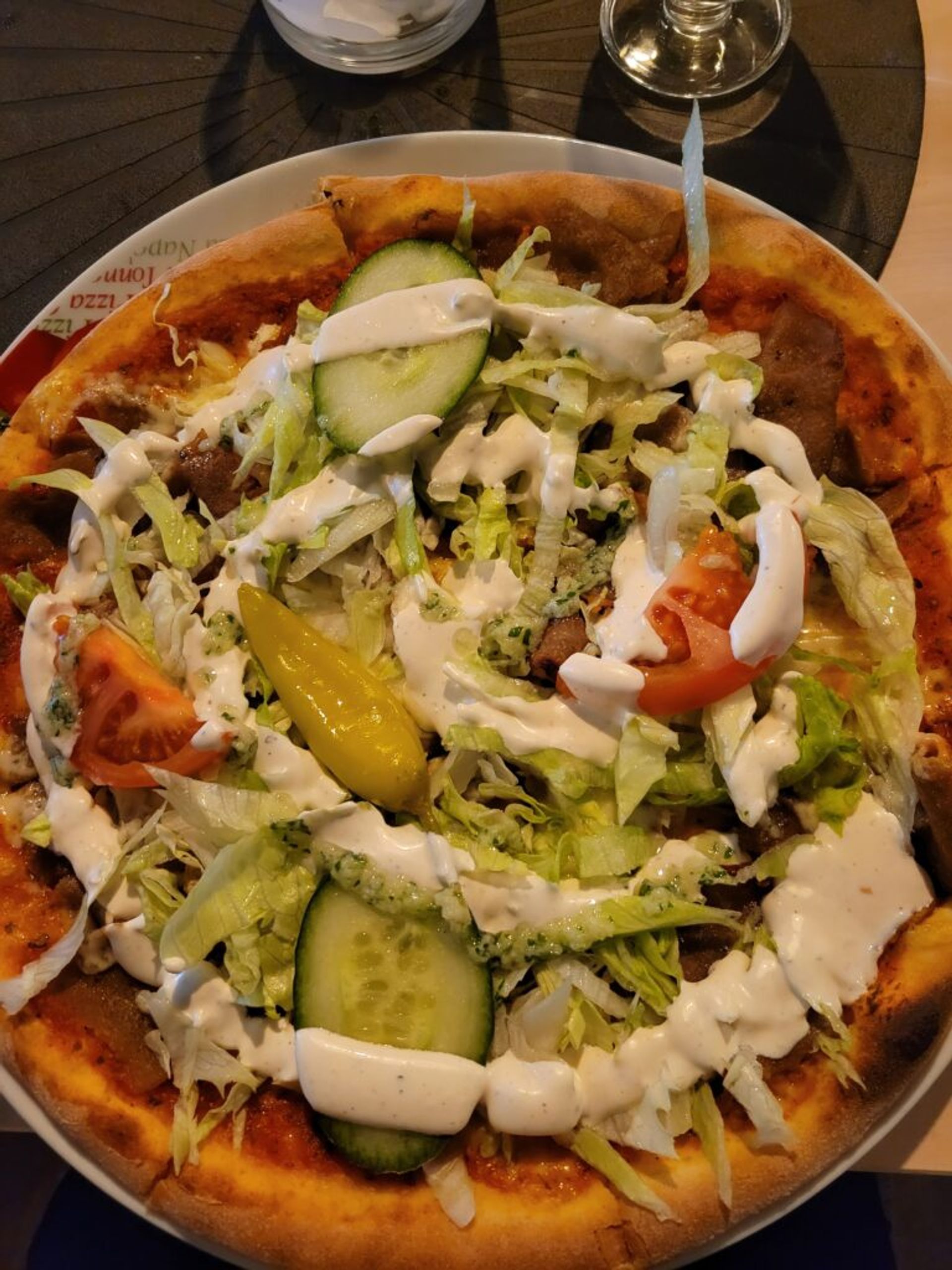 Kebab pizza with cucumbers, tomato, salad, kebab, and sauce.