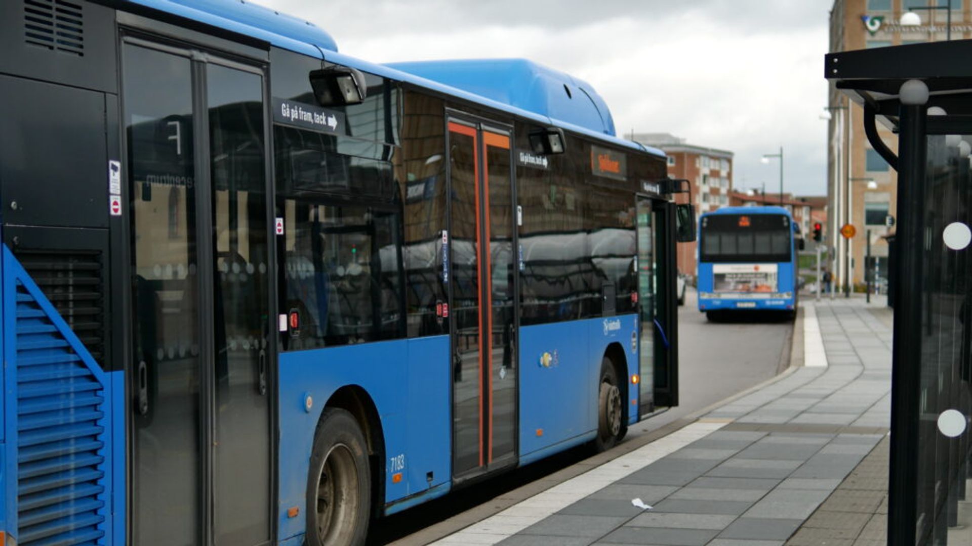 A photo taken of a blue bus waiting by a bus stop in Sweden.