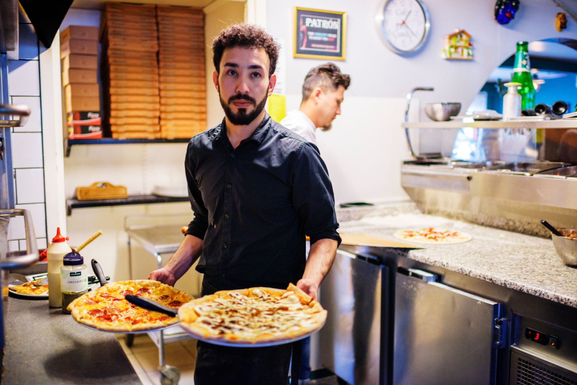 A chef holding two ready-made pizzas at a pizzeria.