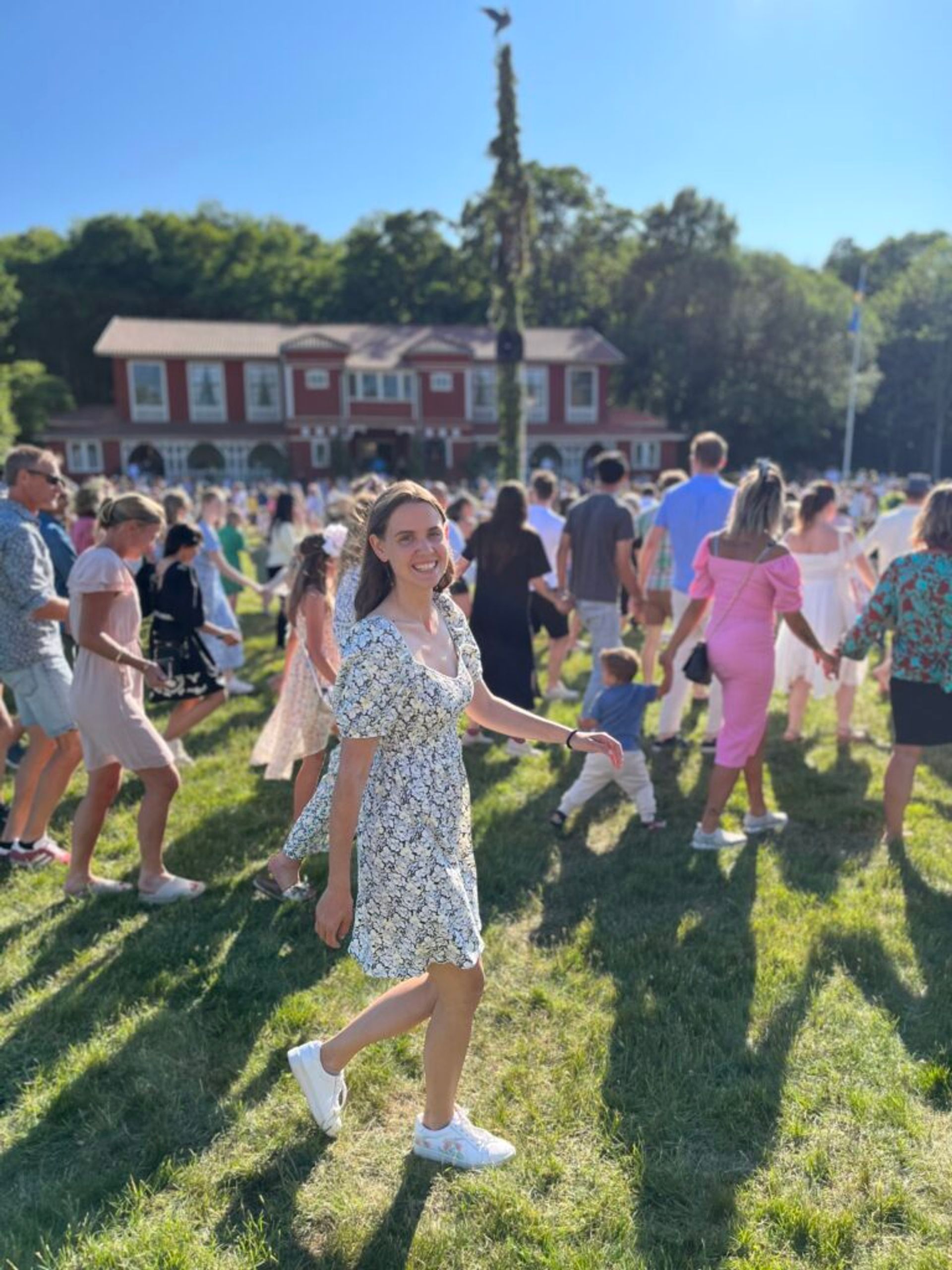 A girl smiling and dancing with a crowd around a Maypole. 