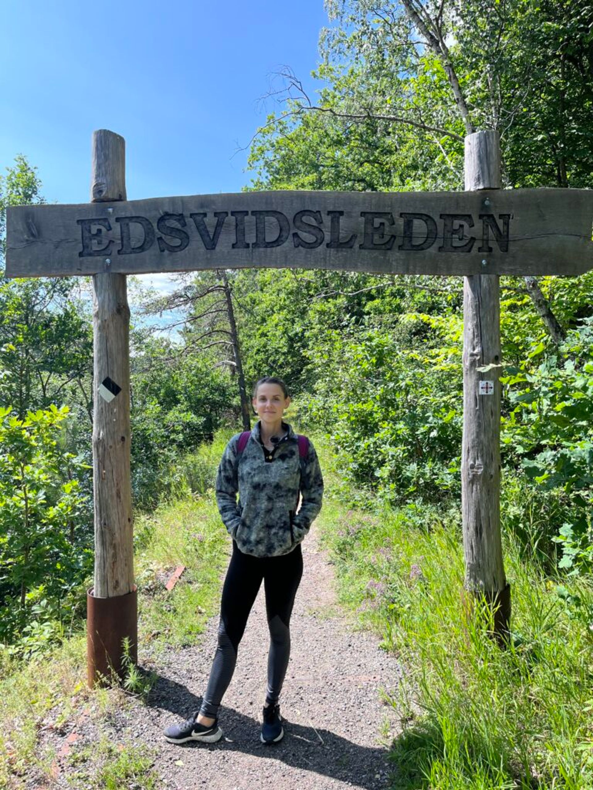 A girl standing under a sign 'Elvidsleden' next to a forest. 