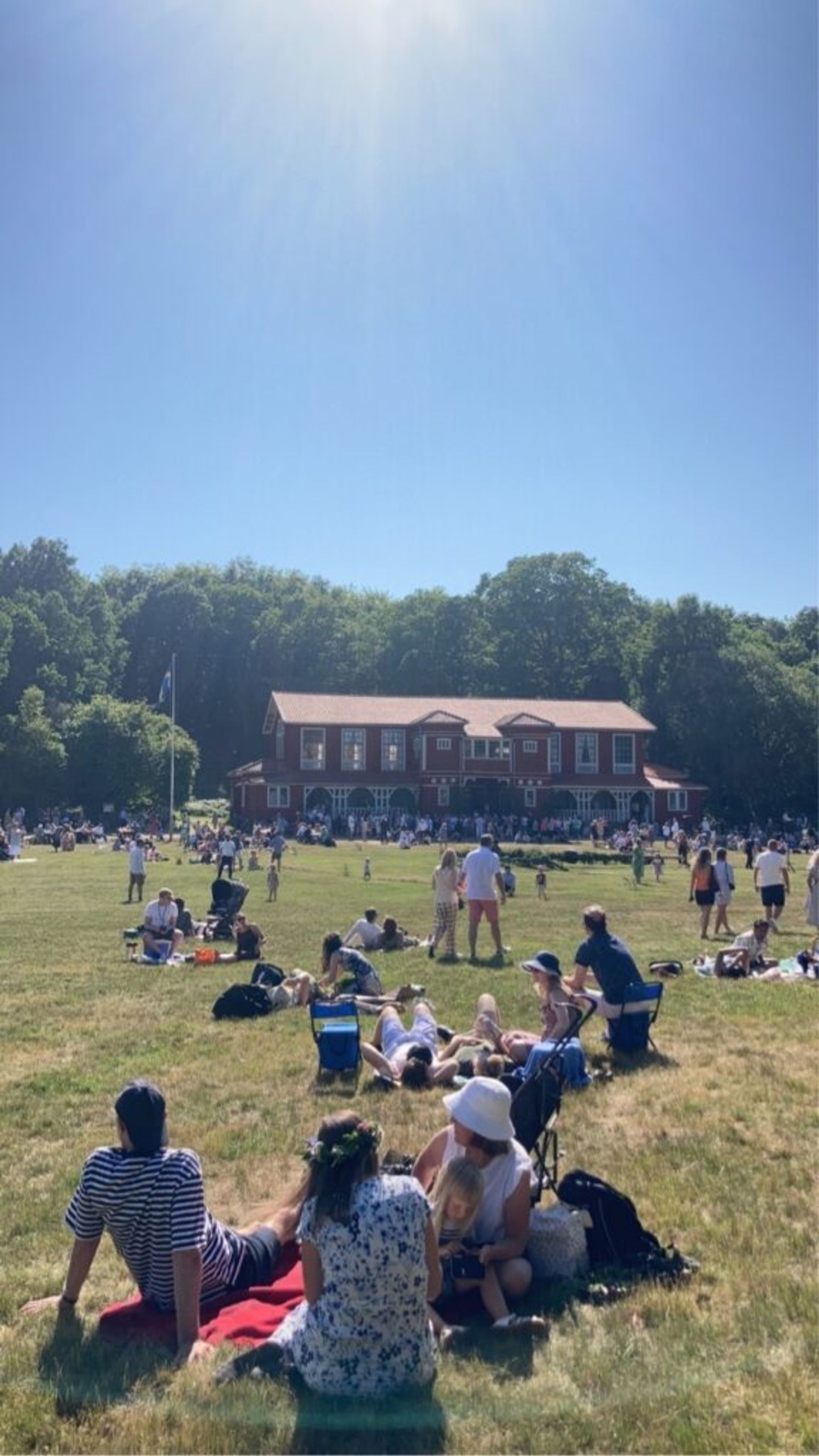 A field with red building and people on a picnic. 