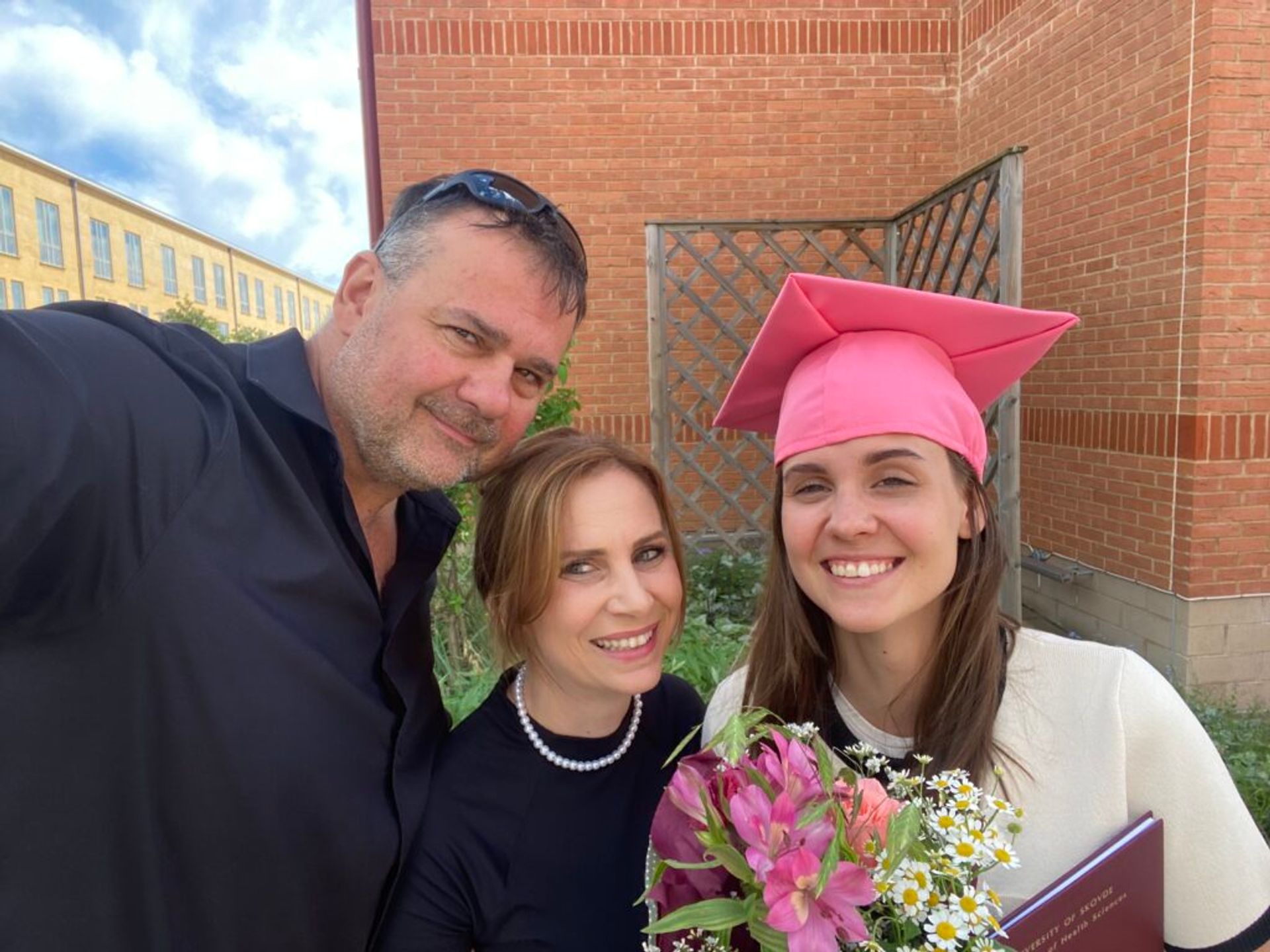 A girl wearing a graduation hat and taking a selfie with mother and father.