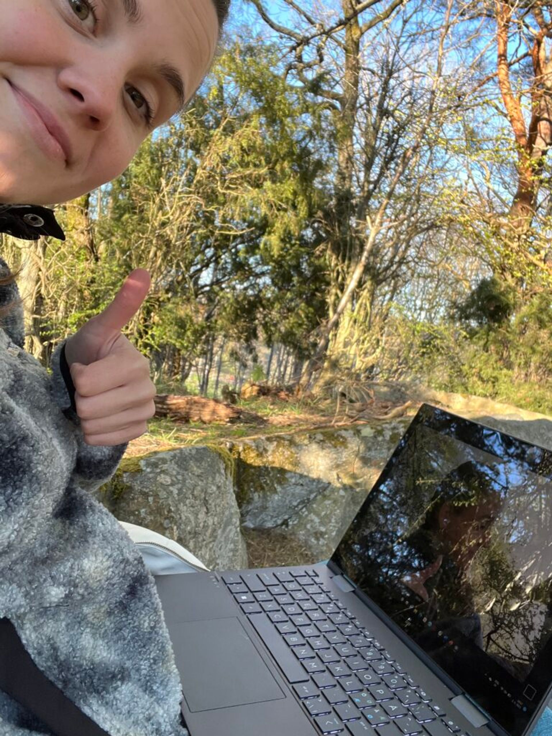 A girl taking a selfie with a computer outside. 