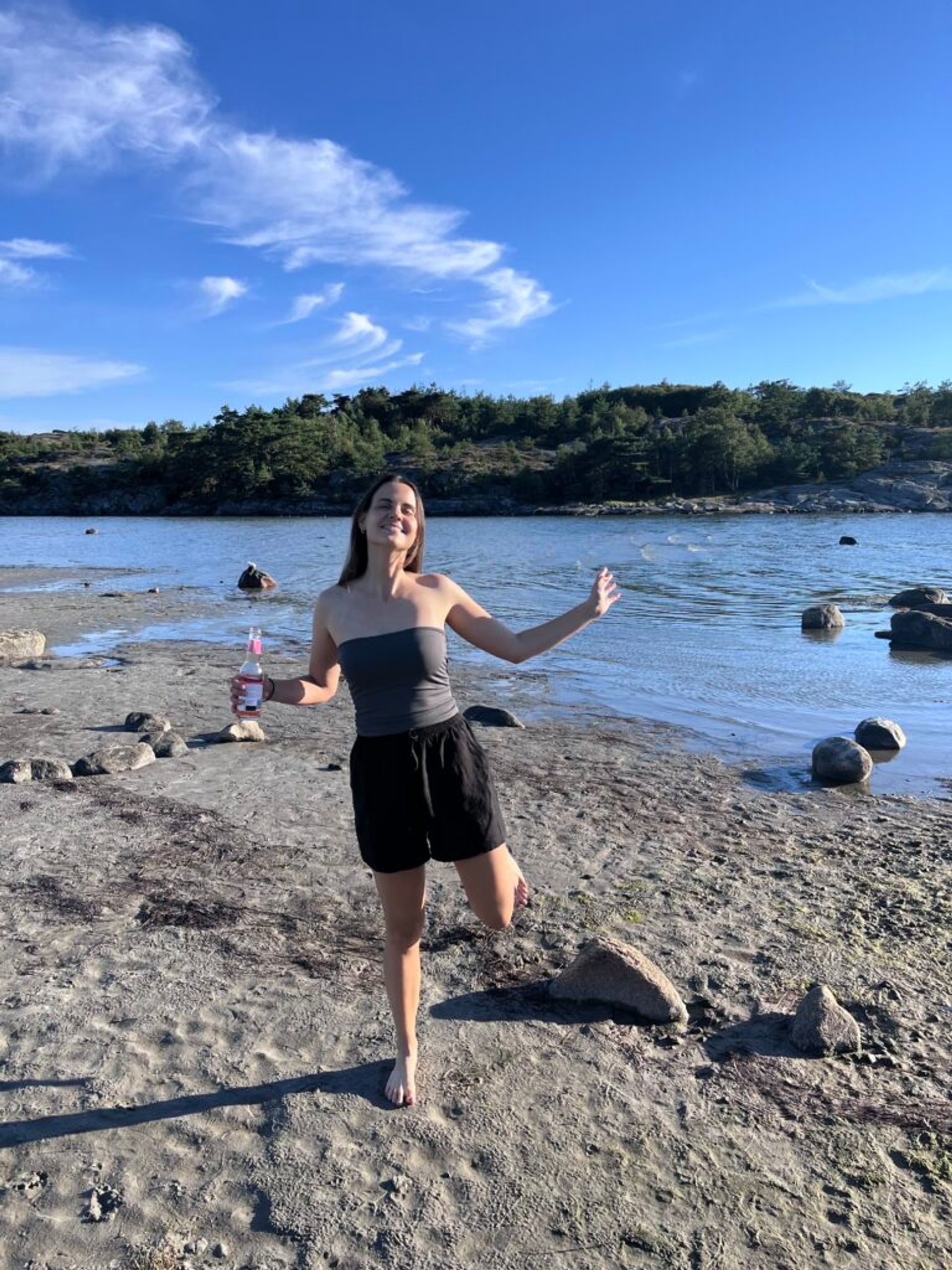 A girl at a beach holding a drink in her hand.