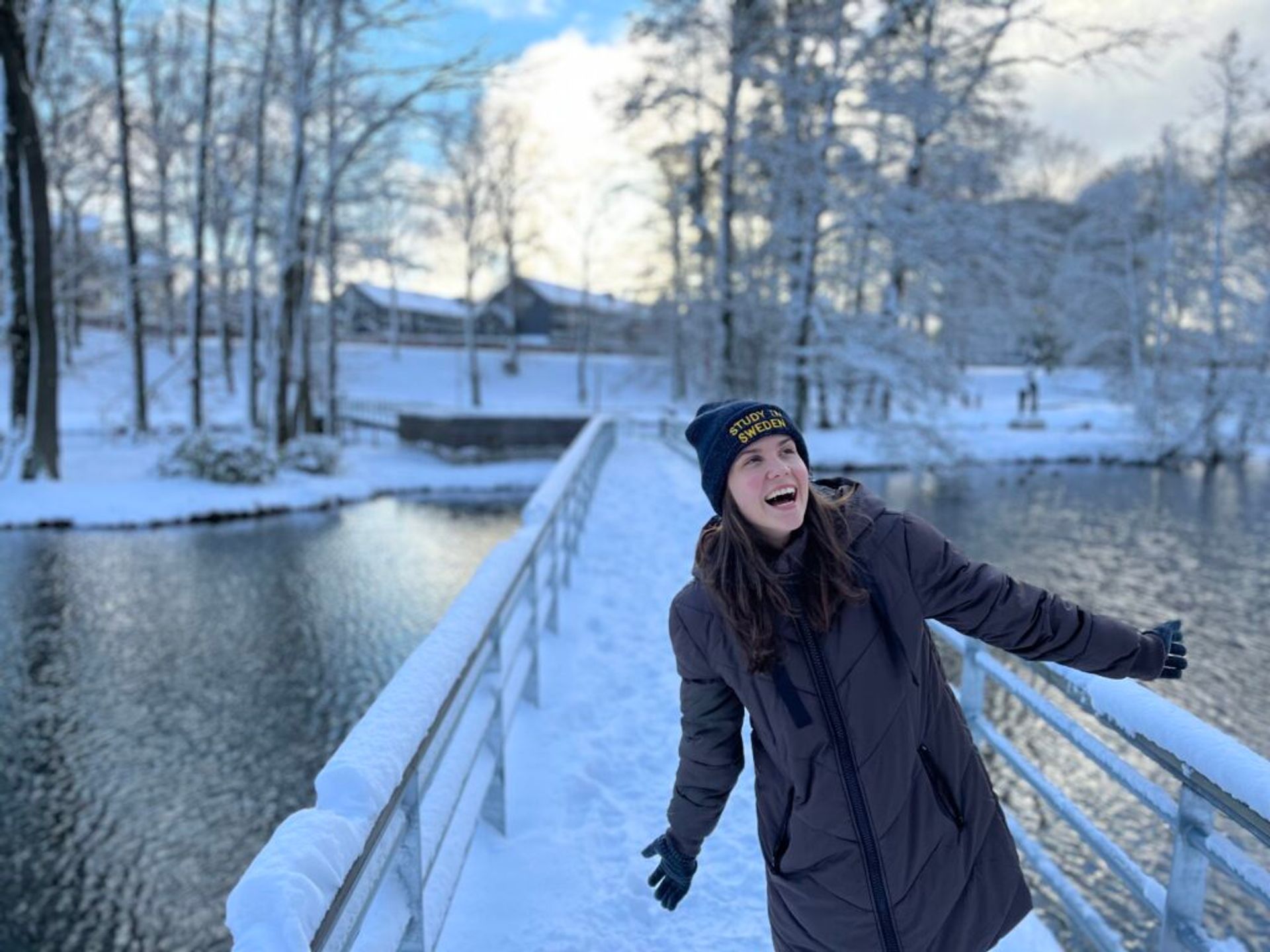 A girl standing on a snow-covered bridge lauging. 