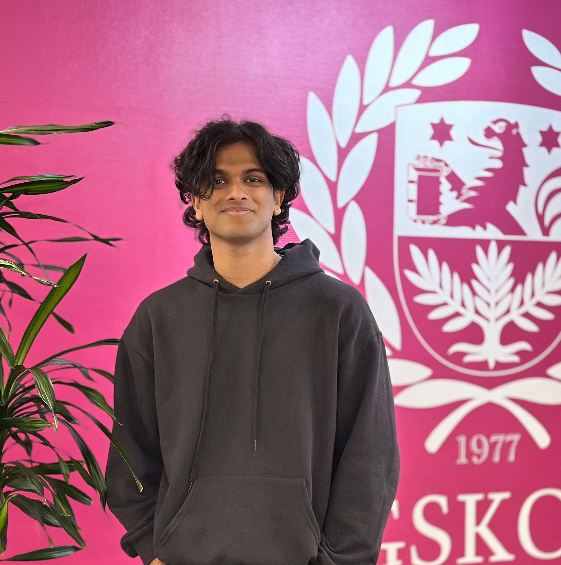 A boy standing in front of a pink wall with the University Emblem