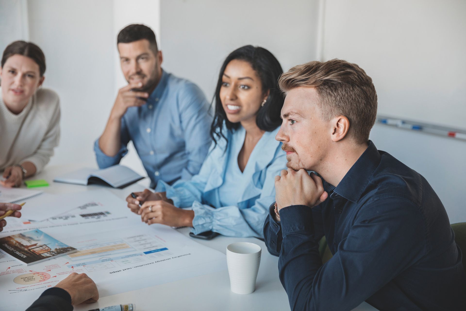 People are sitting around an office desk filled with sheets of paper. They all look in the same direction.