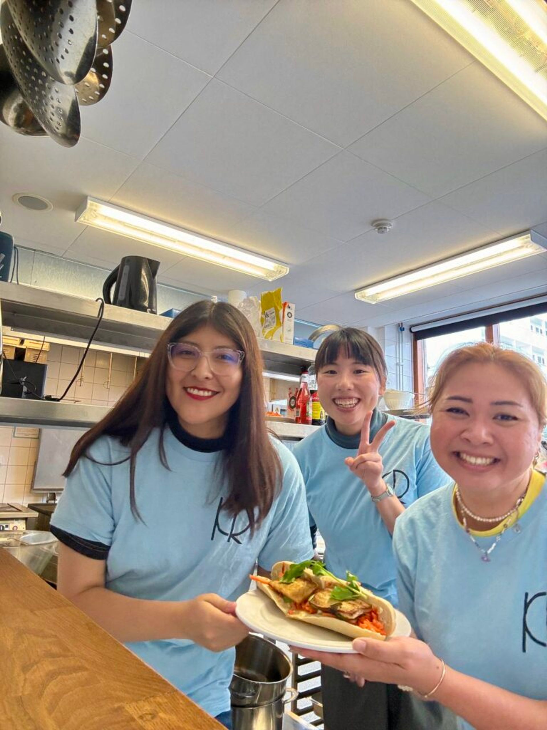 Three woman smiling at the camera with a sandwich in their hands