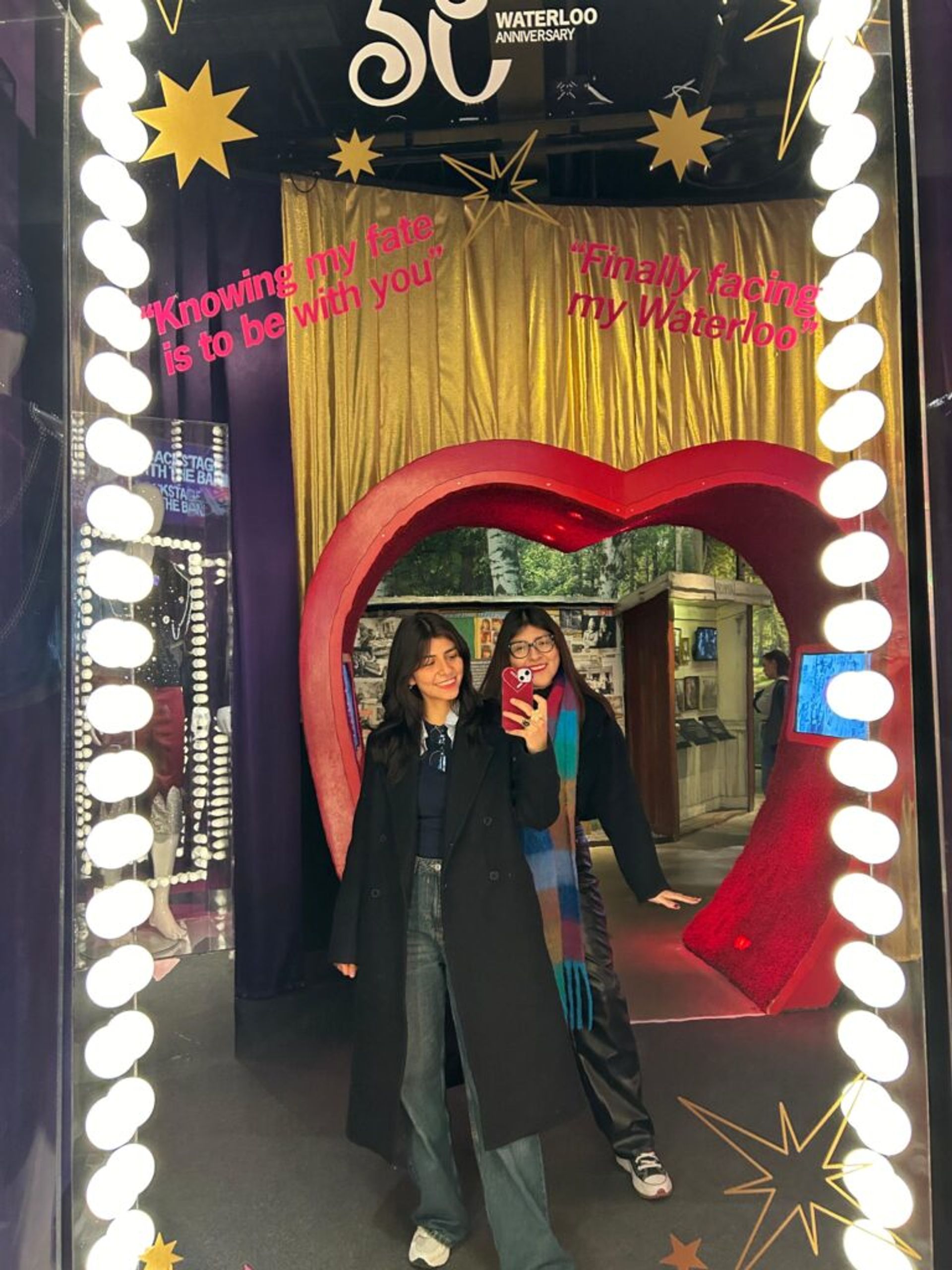 Two girls smiling at the camara in front of a mirror.