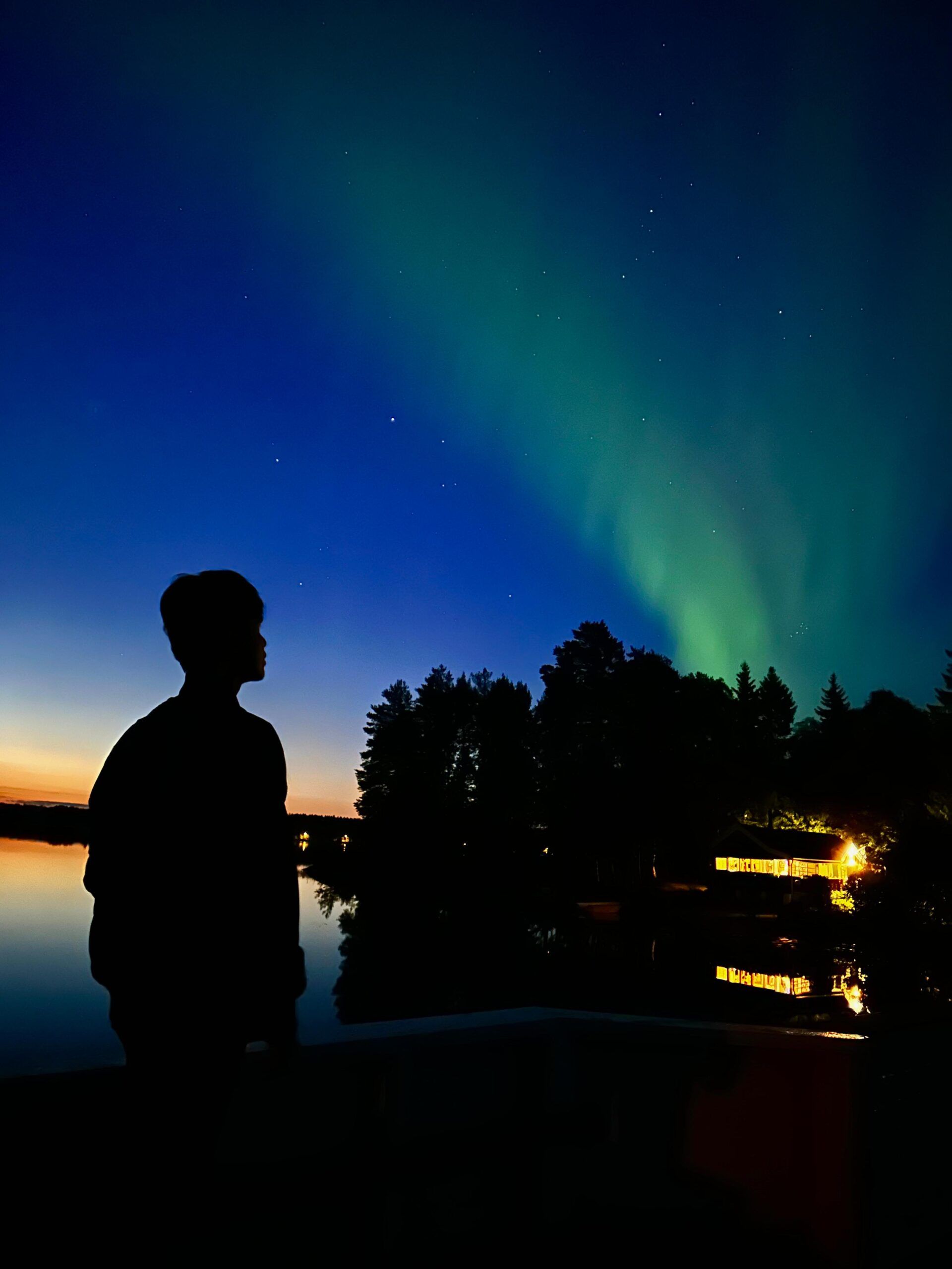 the dark silhouette of a boy looking at the night sky filled with Northern lights