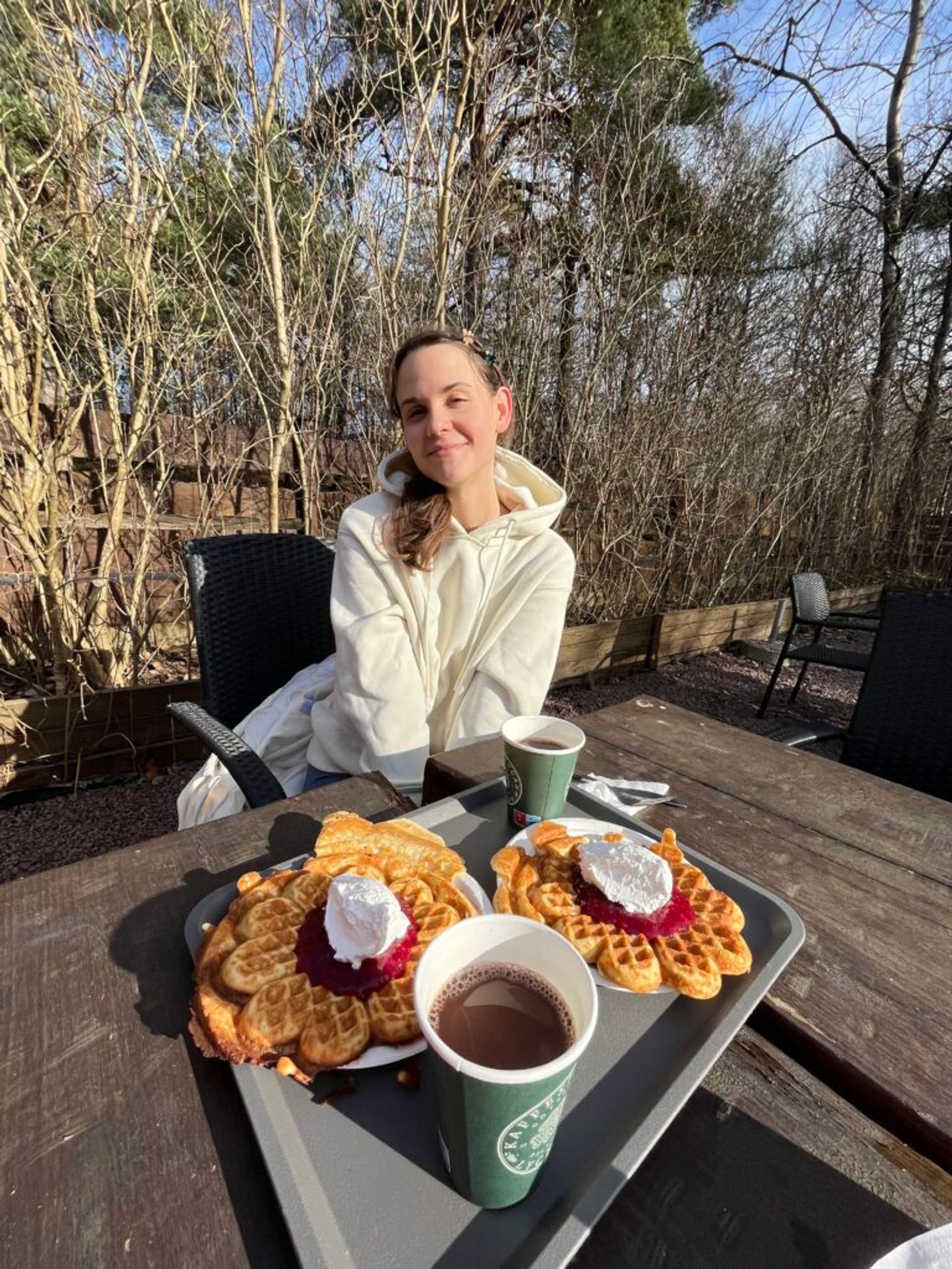 A girl with plates with waffles on a table outside.