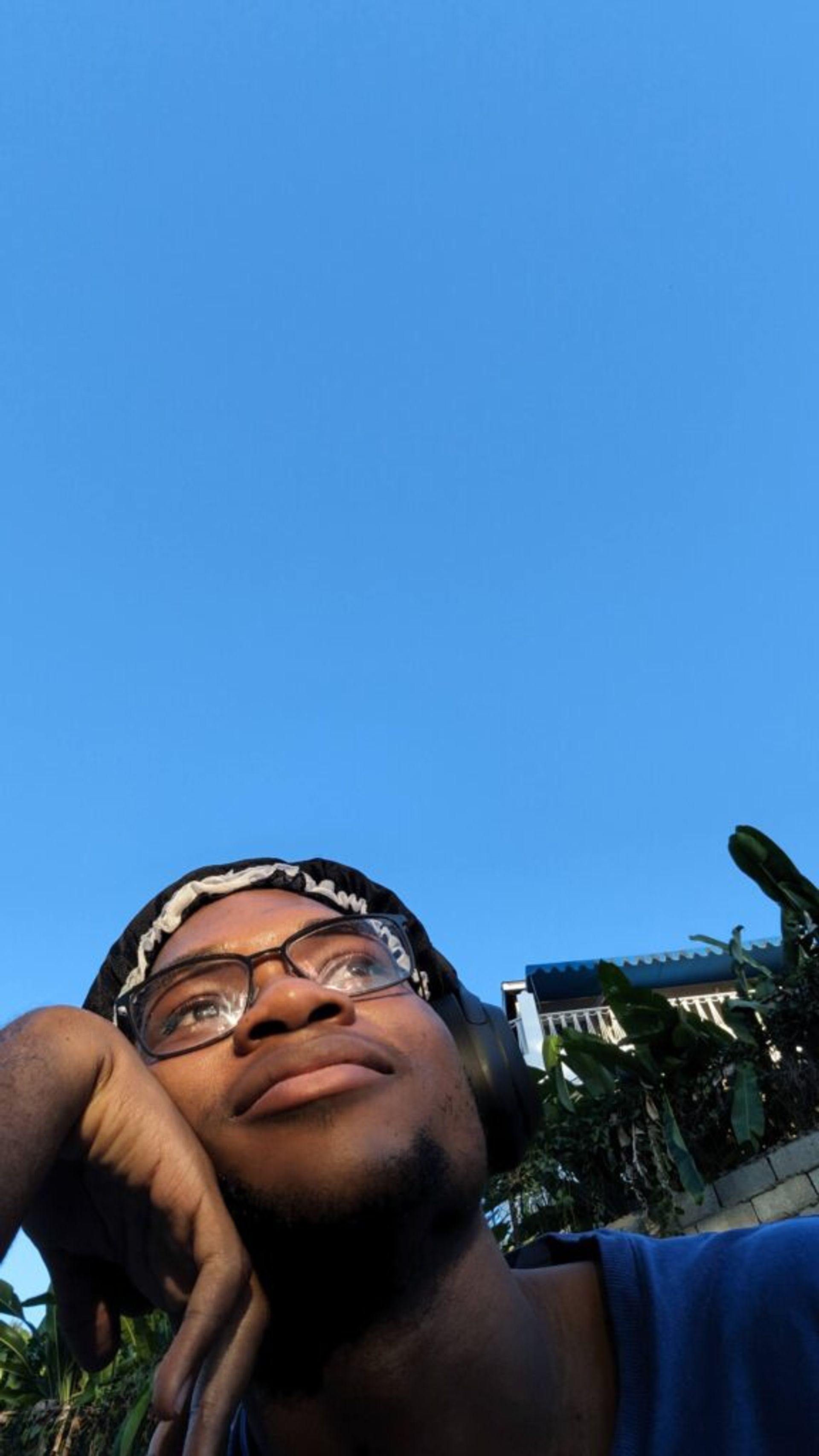 Picture of Joshua in his bonnet sitting in his yard with his cheek resting on his hand looking into the sky with the afternoon sun in his face. 