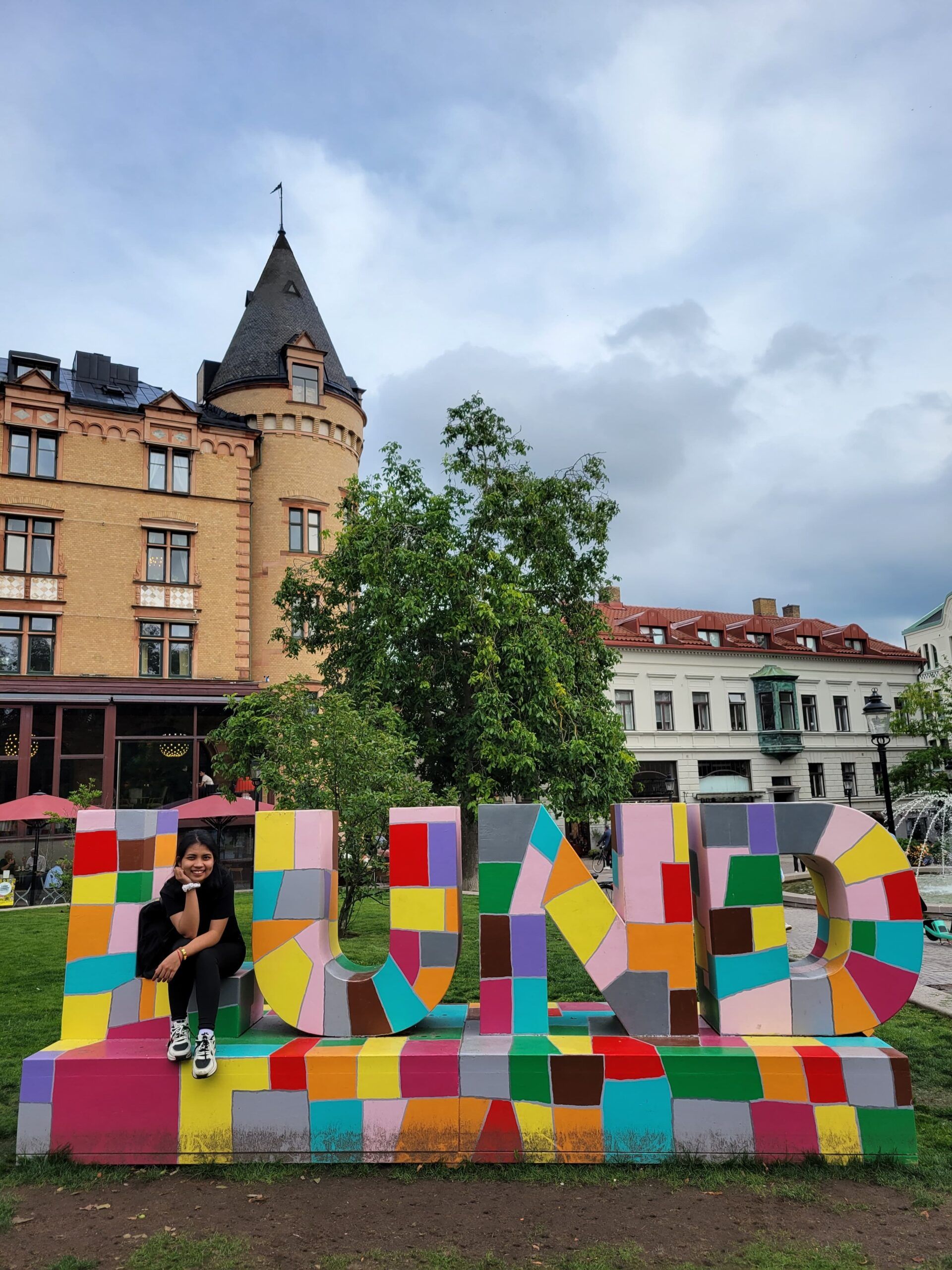 A girl sitting on a large colorful structure spelling out "Lund"