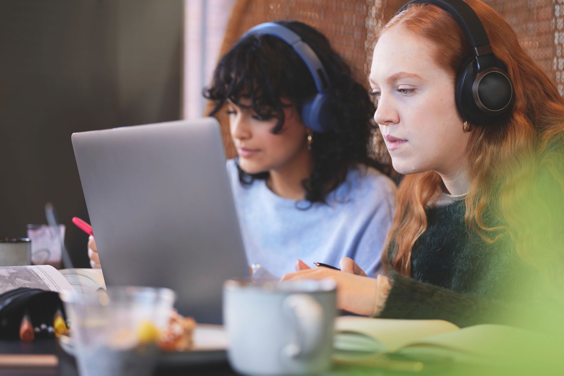 Two women with headsets and computers by a desk.