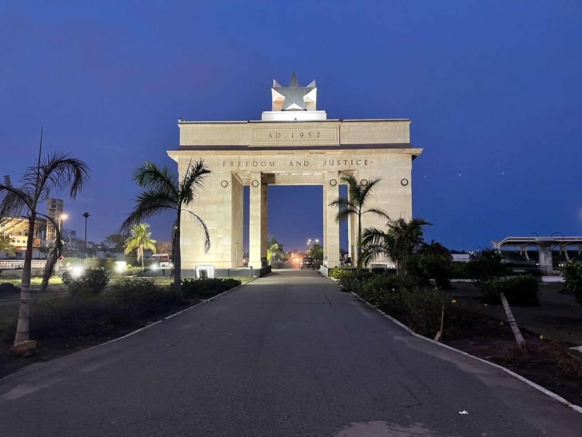 Photo of the Black Star Gate, a monument in Ghana. The monument is a rectangular arch build with beige stones. Freedom and Justice is written on the face of the monument and a black star sits on the top.