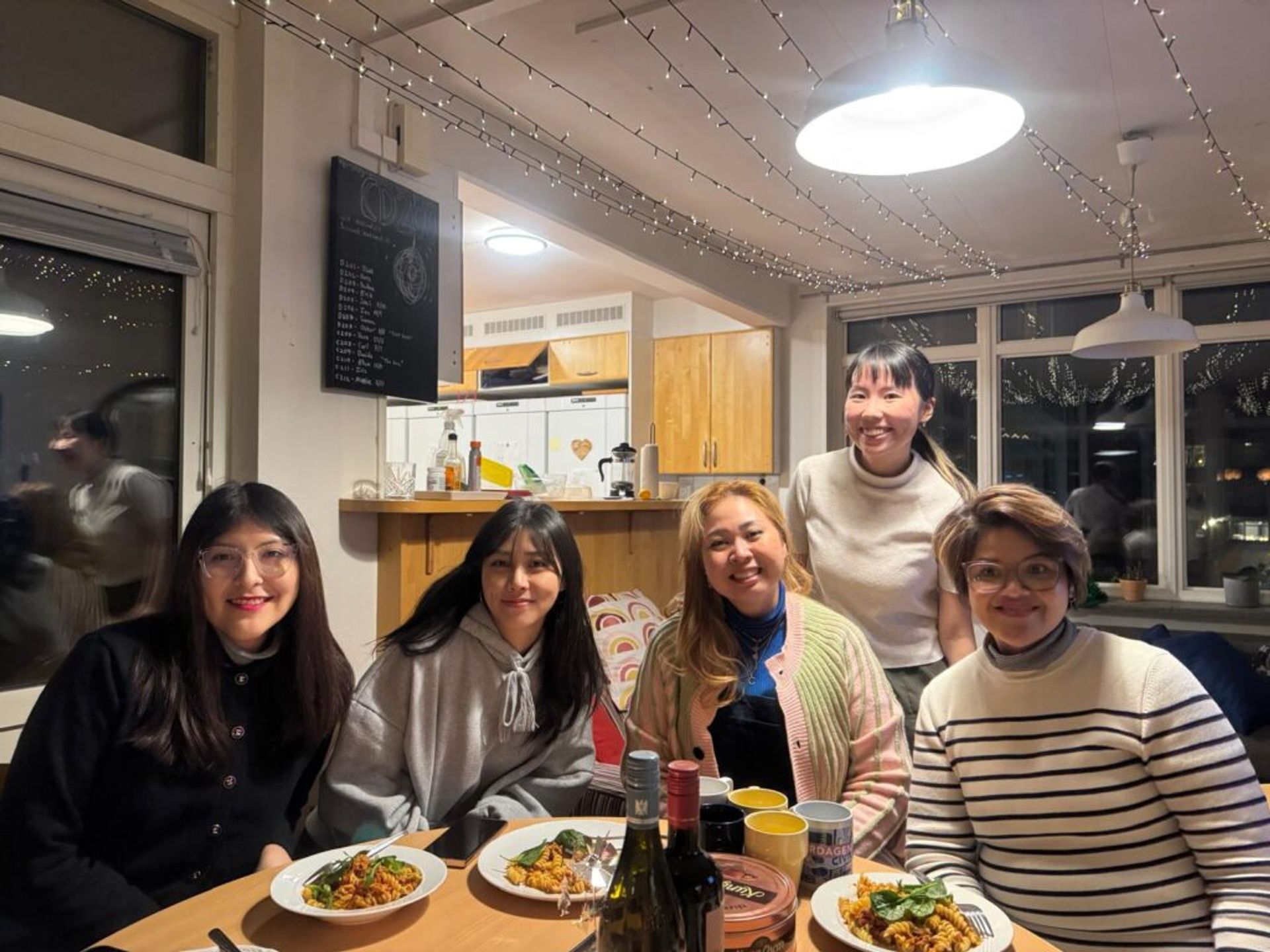 Five girls smiling at the camera while having a table with dinner to eat