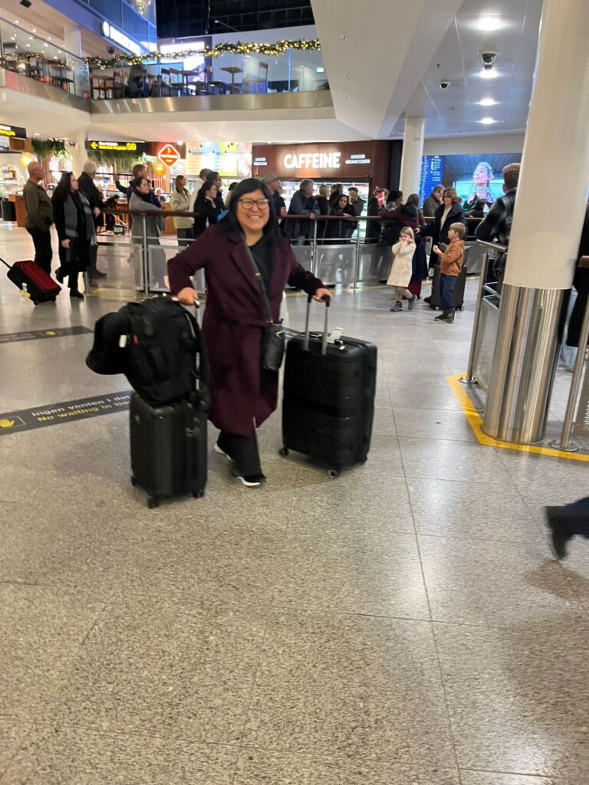 A woman arriving in a airport with two suitcases.