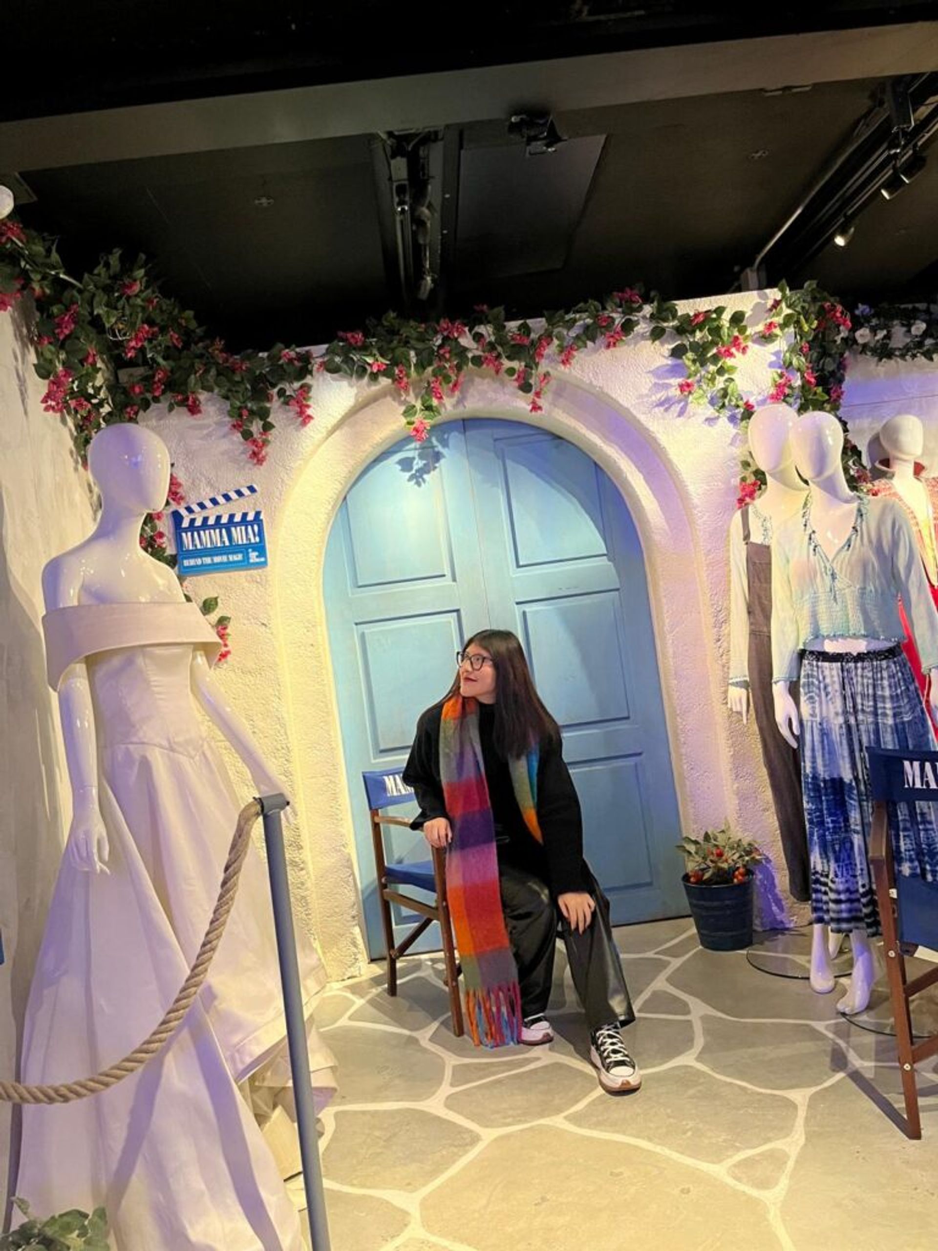 A girl seated in a bench of a Mamma Mia set in a museum.