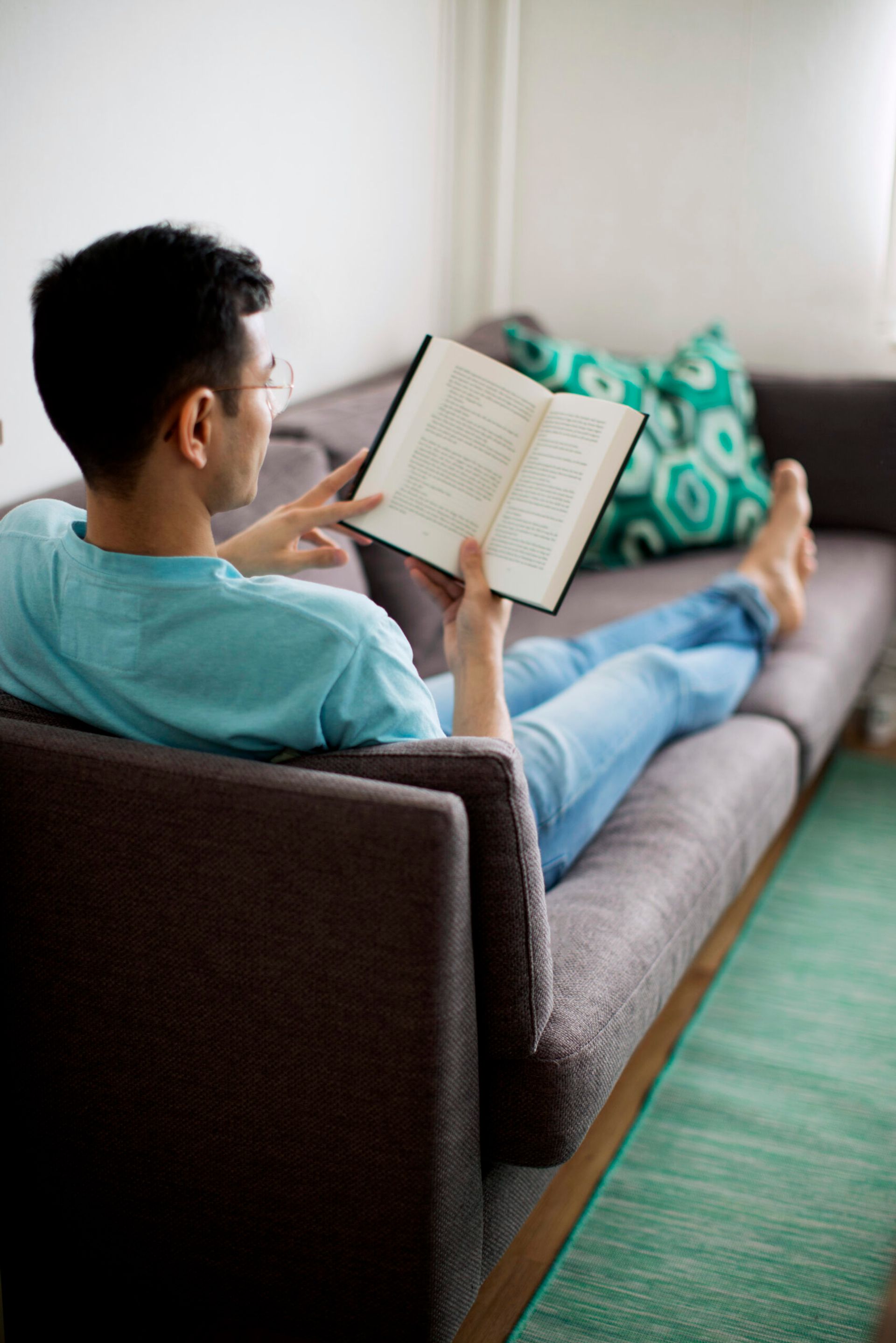 A student reading book while laying on a couch