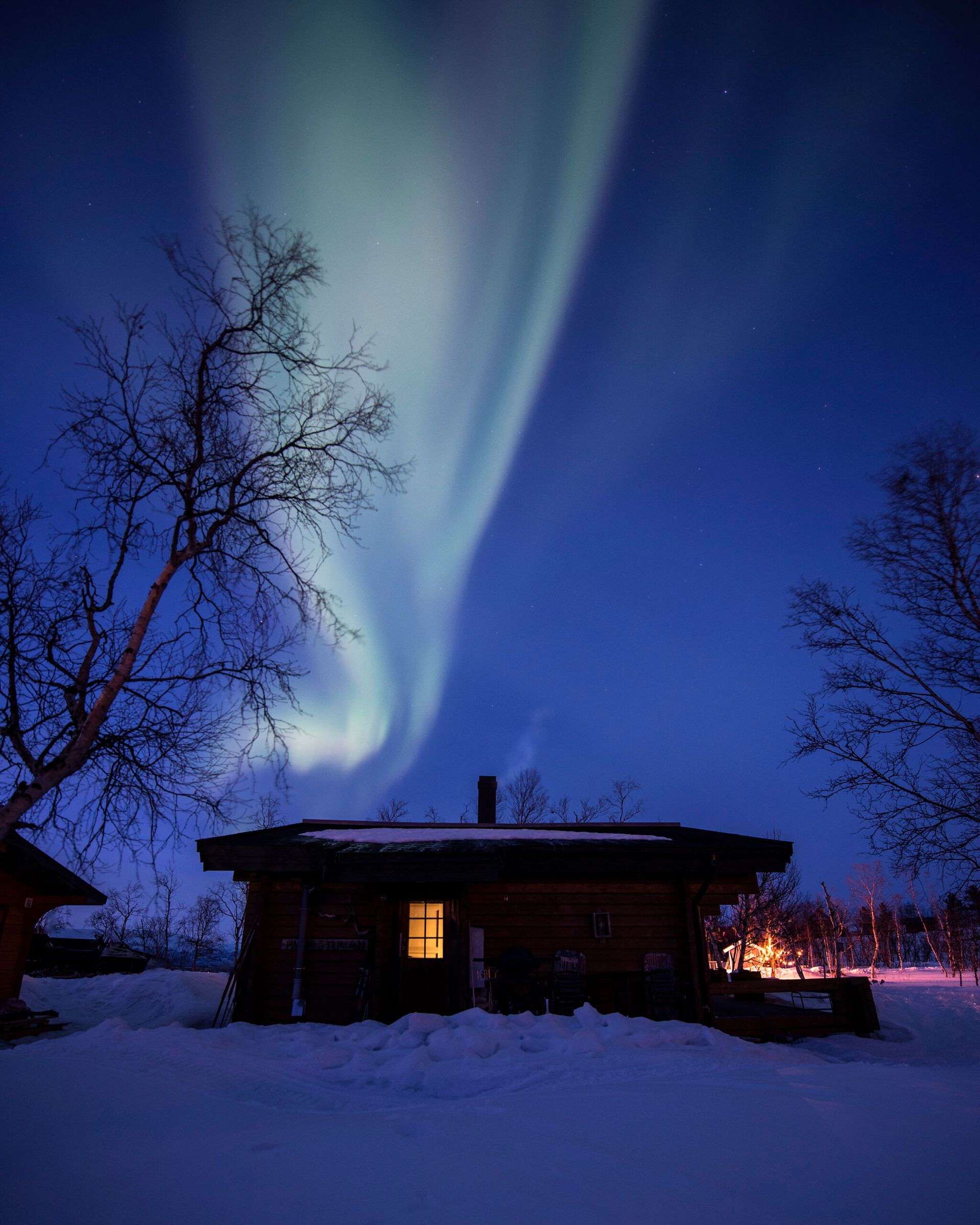 An exterior shot of a cottage in the dark with the green northern lights in the sky