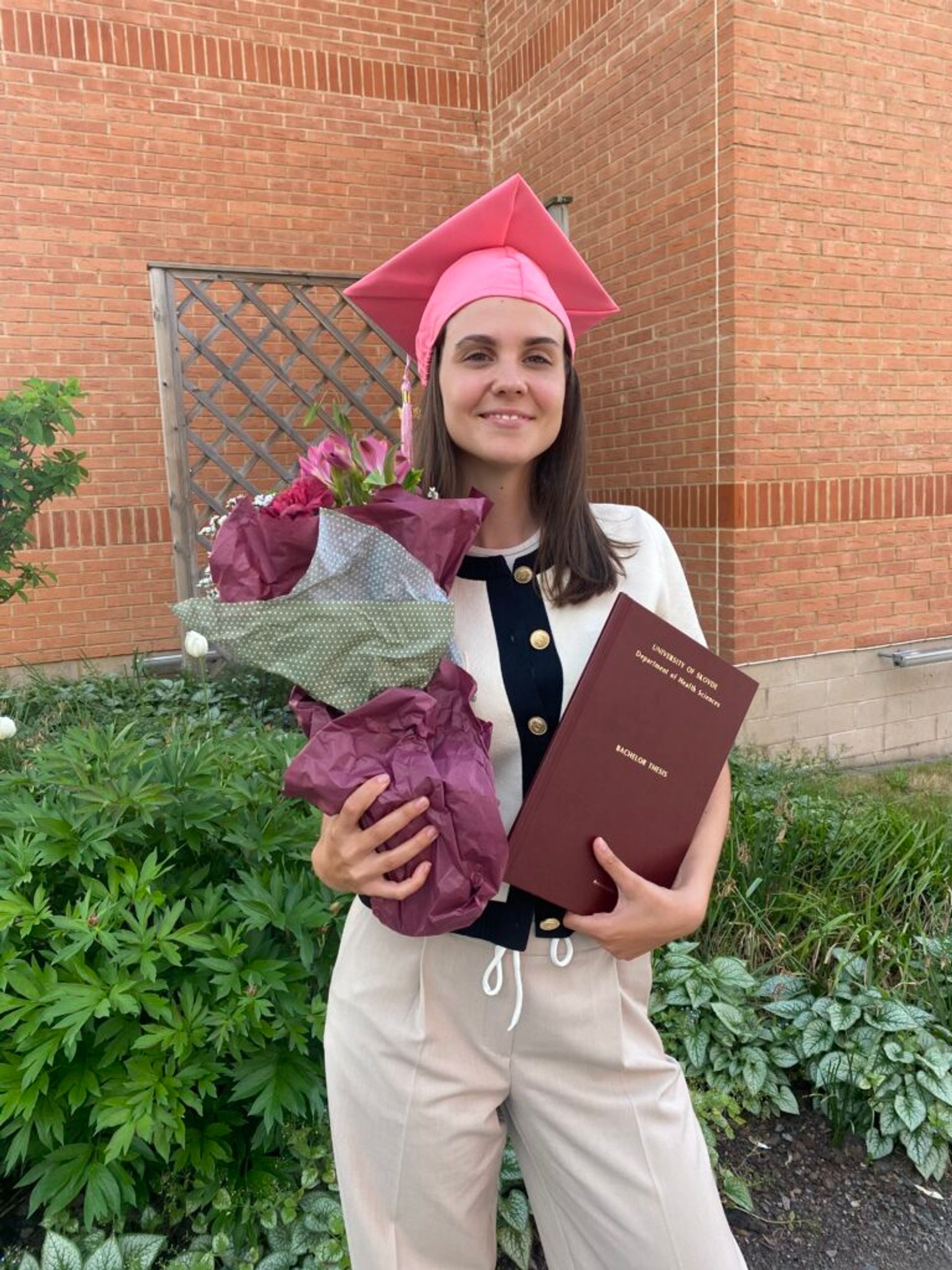 A girl wearing a graduation hat and holding flowers.