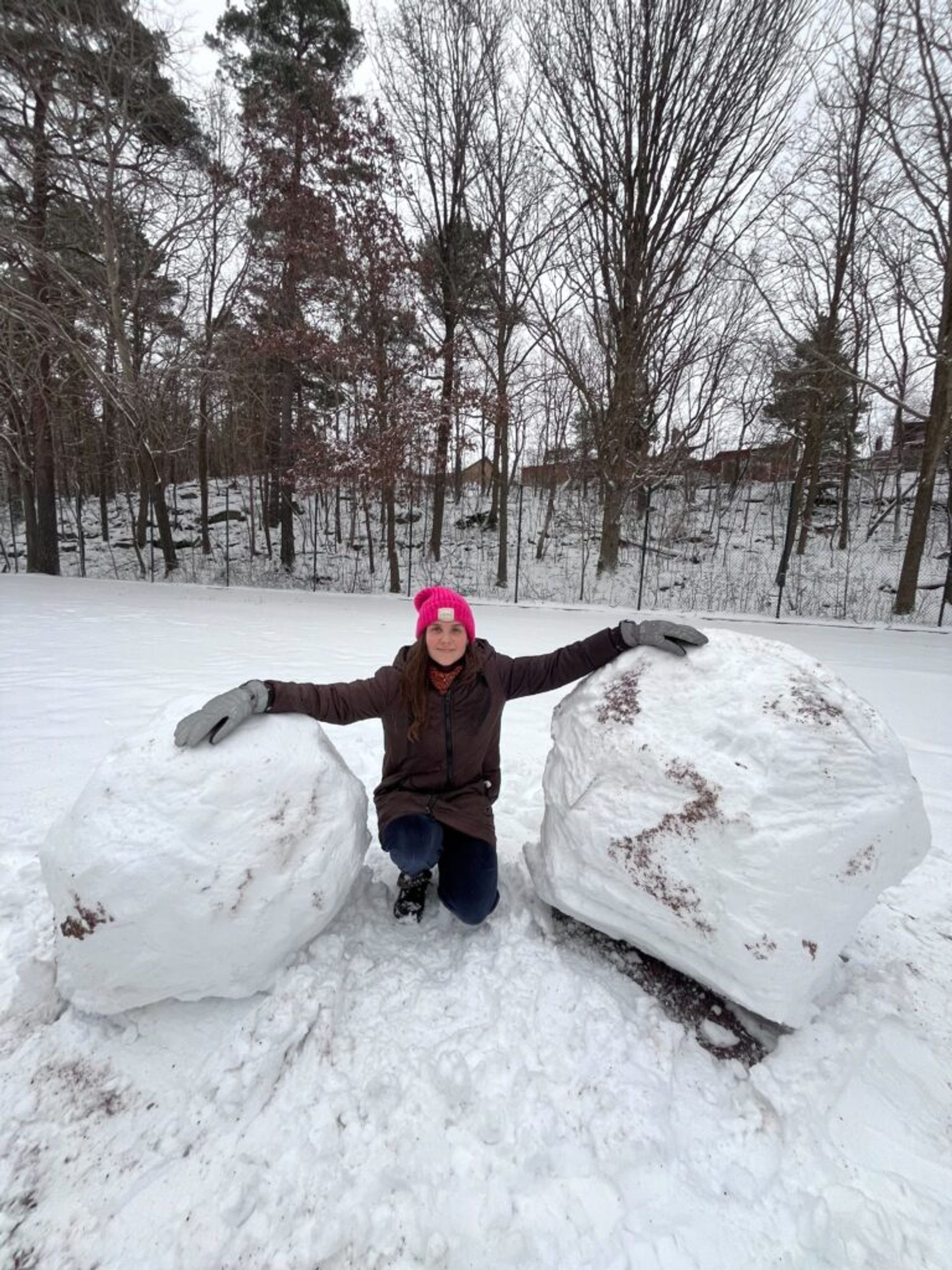 A girl posing with two large snowballs.