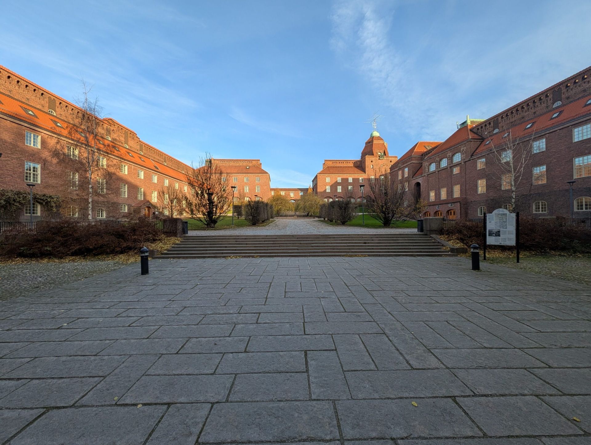 Picture of a courtyard between 3 red brick building in the sunset. The glow of the sun is on the tops of the two buildings to the left of the courtyard.