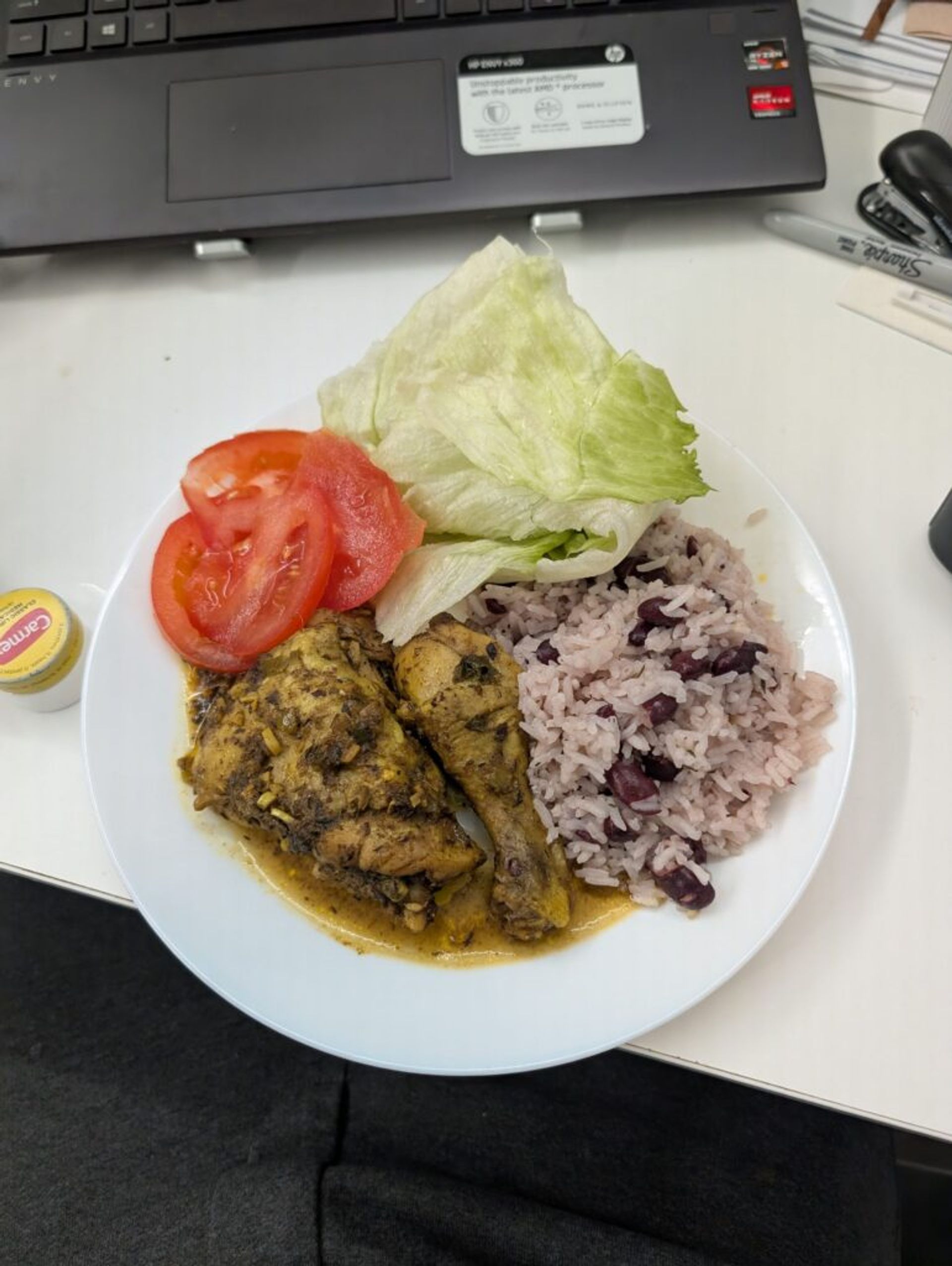 A picture of a plate with traditional Jamaican rice and peas, Jamaican curried chicken, lettuce and tomatoes.