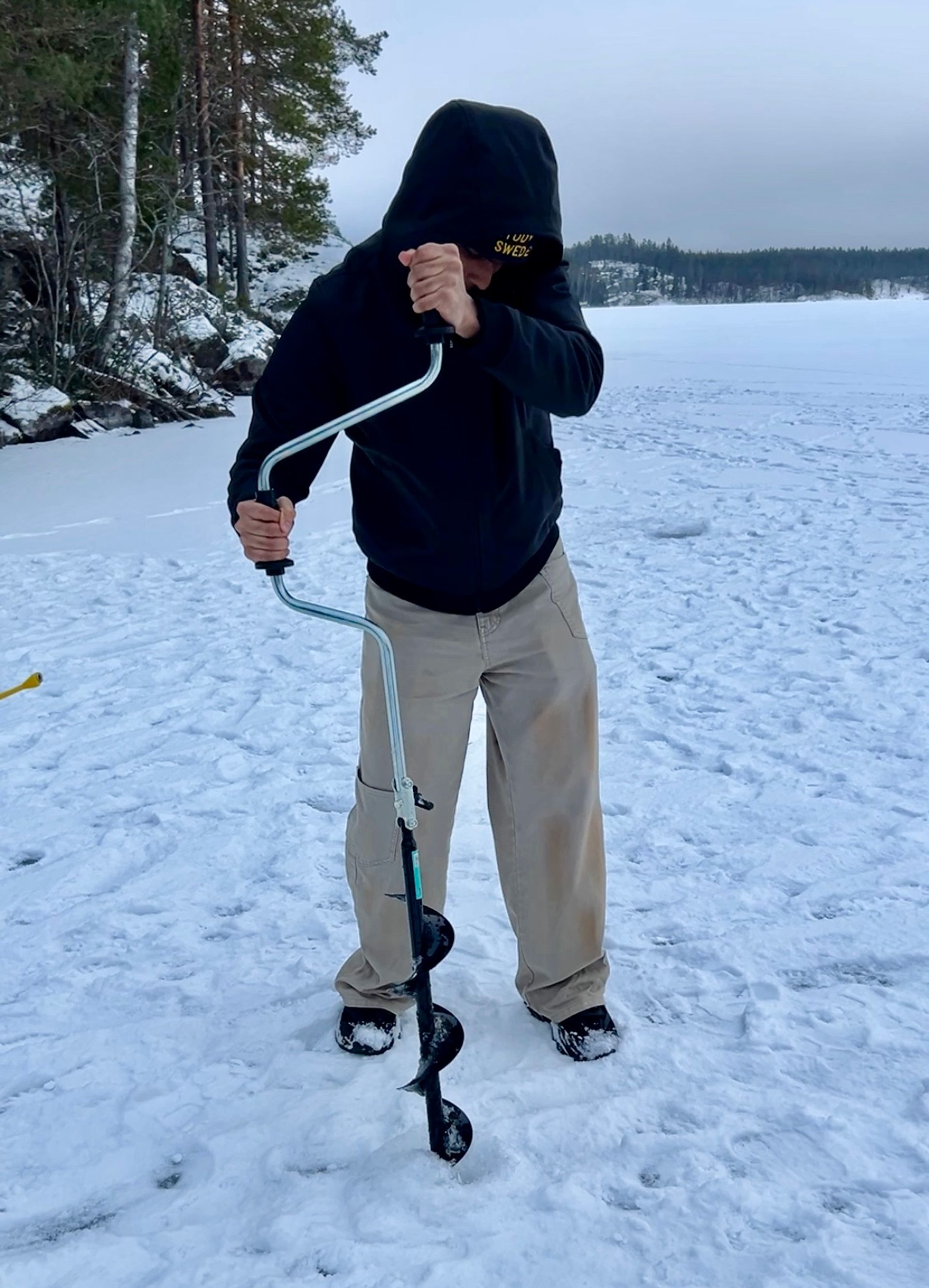 a boy drilling a hole in a frozen lake