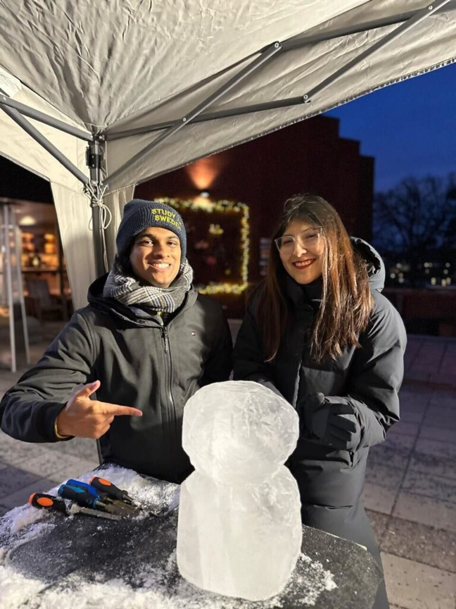 A guy and a girl smiling and pointing on an ice block. 