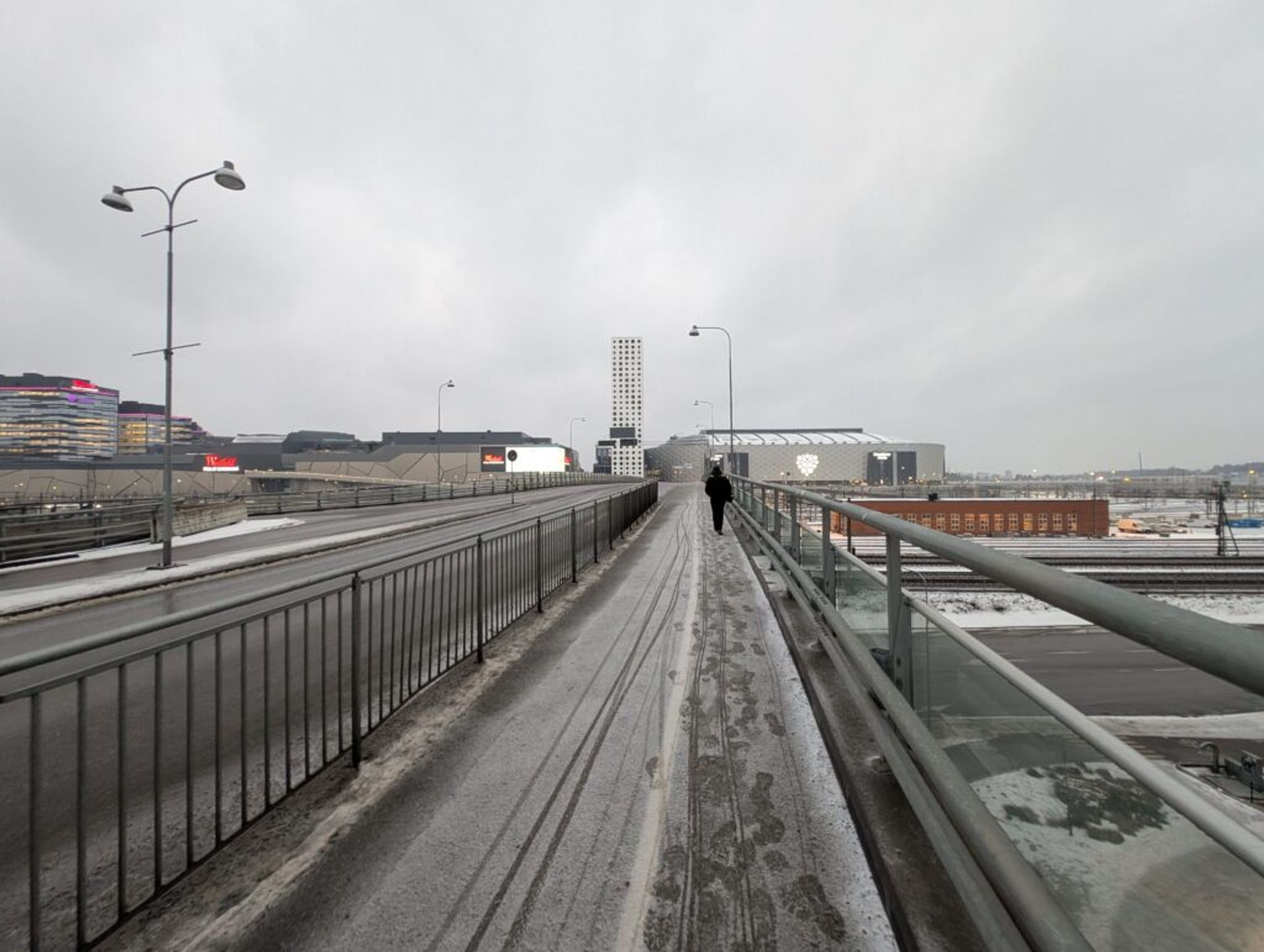 A picture looking across a highway bridge with light snow on the ground. There are many large buildings in the background and the sky is gray and cloudy. 