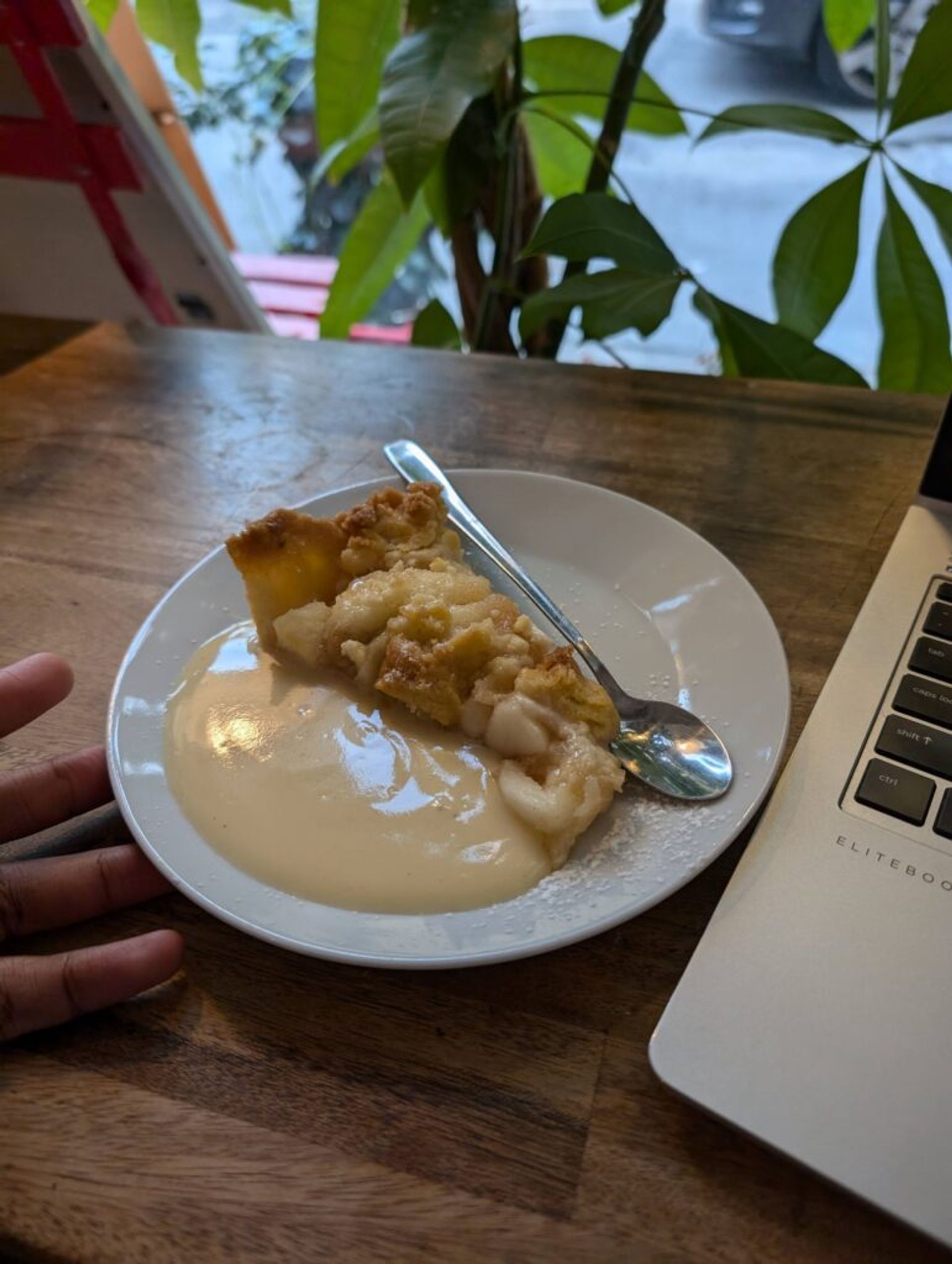 A slice of apple pie on a white plate with cream on the side. The are large slices of apple in the pie. 