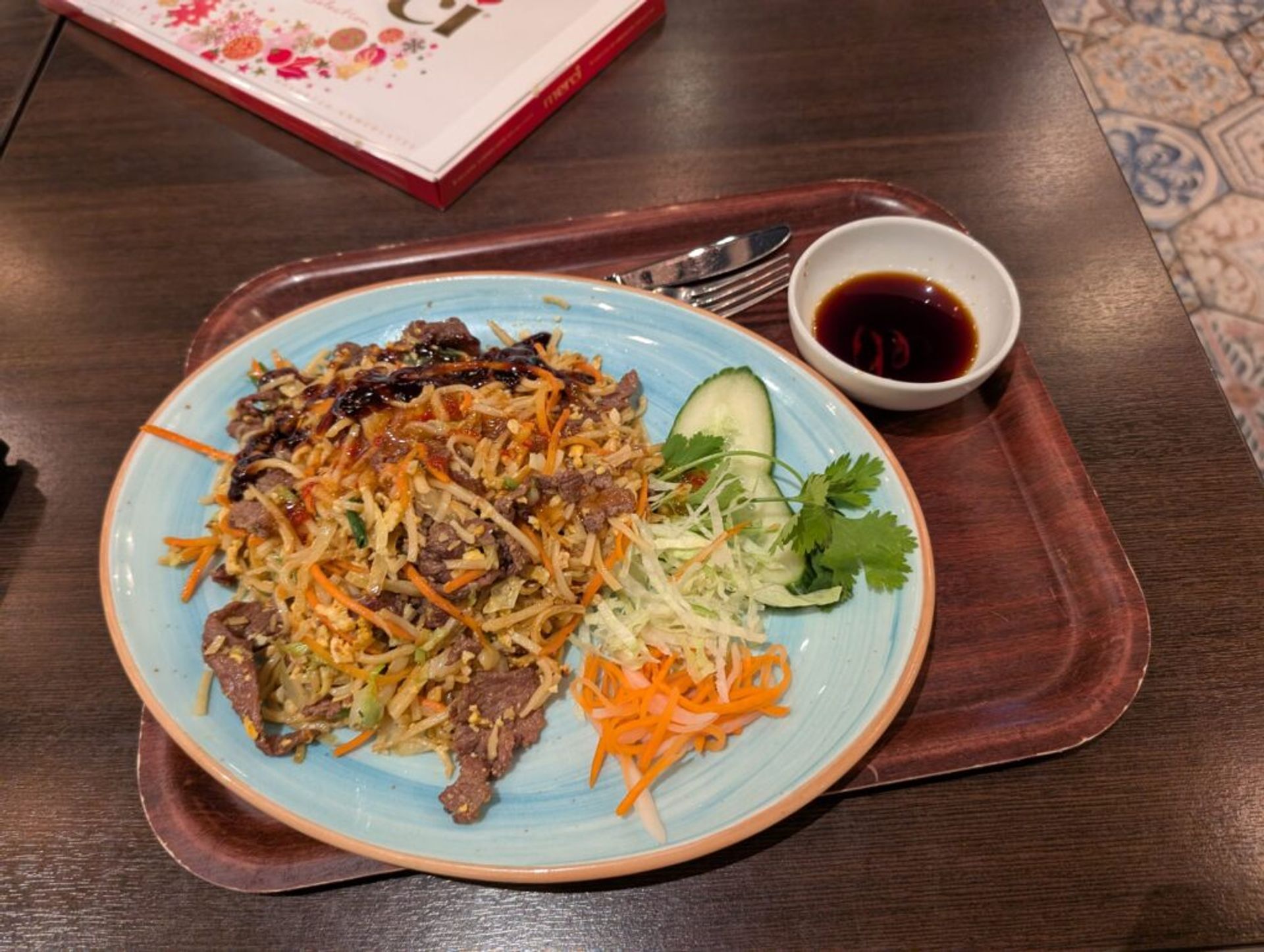 Thai food in Sweden. There is a mix of noodles, carrots, cucumbers, lettuce and asparagus on a plate and soy sauce in the corner. 