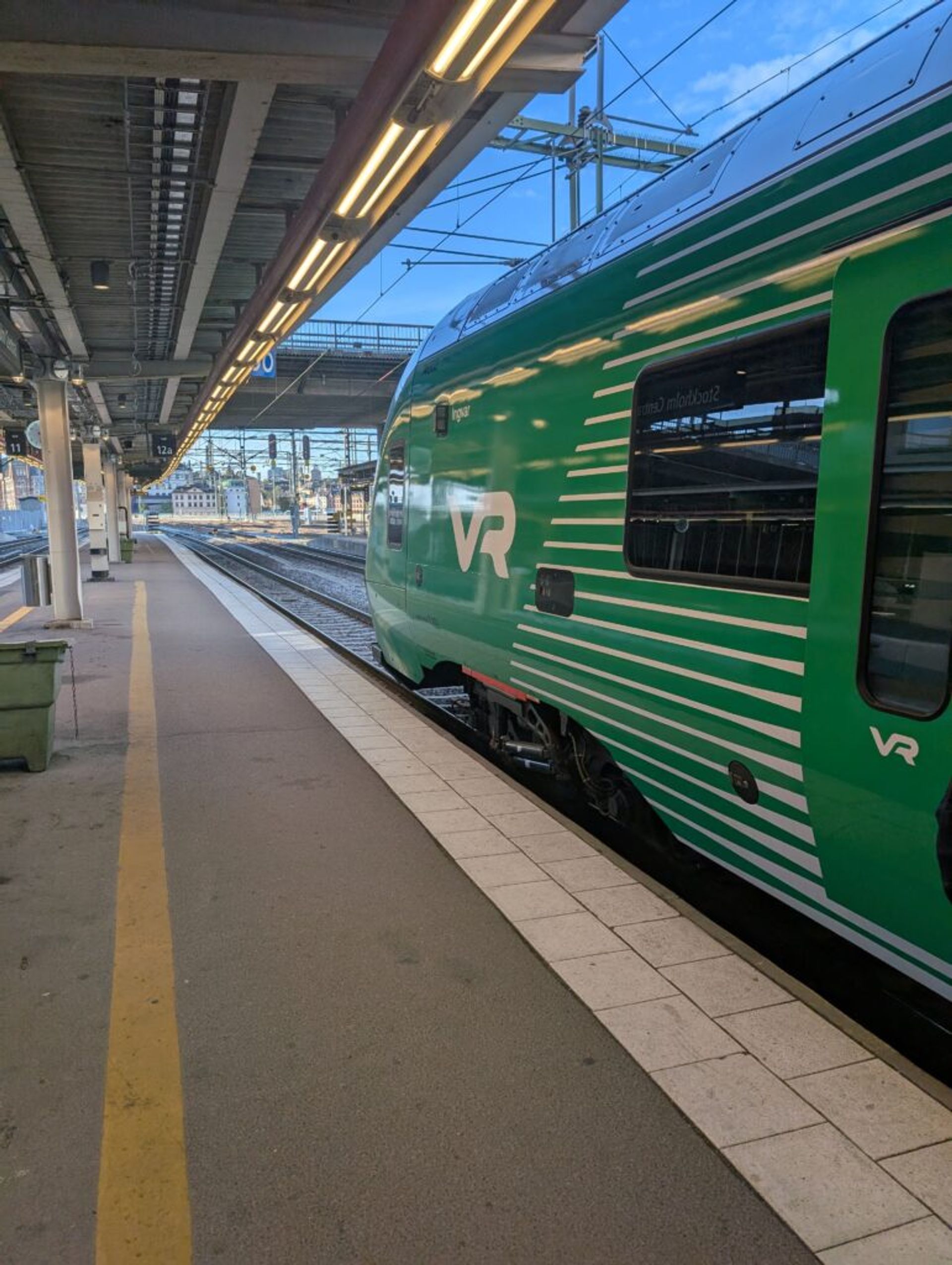 A photo of a high speed train on at the platform at Stockholm Central Station. The train is labelled with the VR logo and covered in a green wrapping.