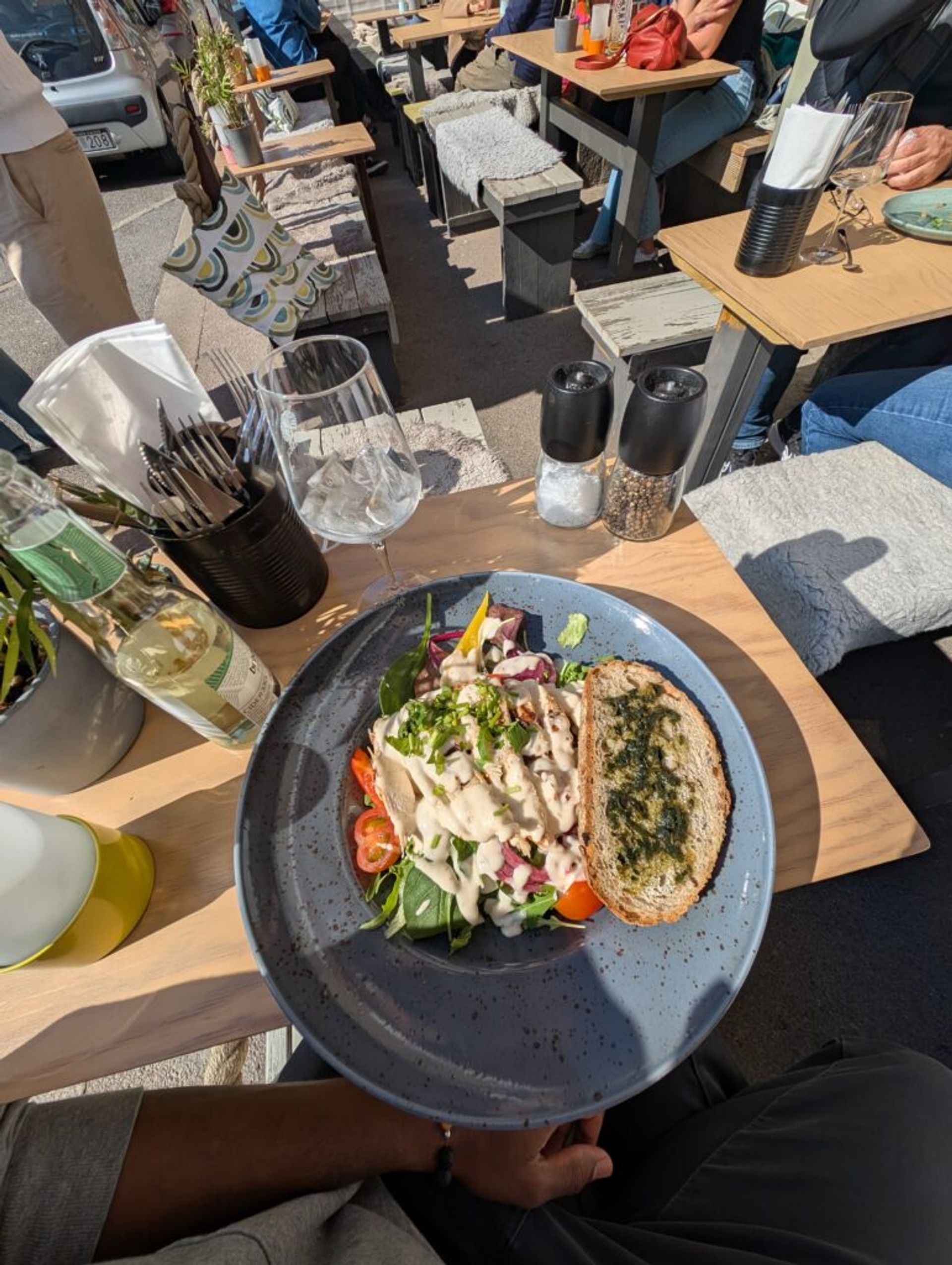 A picture of a table with a gray plate. on the plate is a chicken salad covered in dressing, along with a slice of garlic bread.