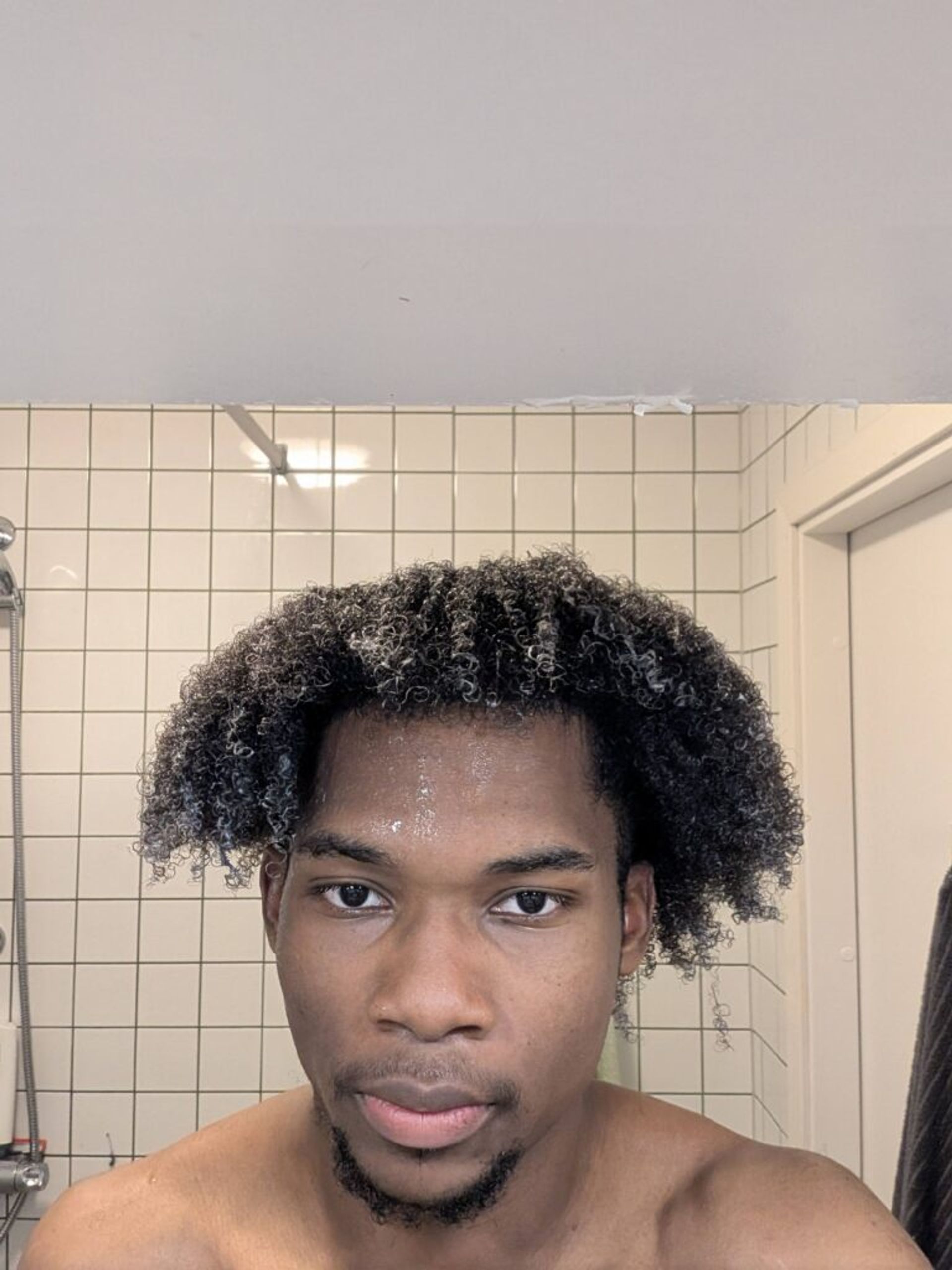 A selfie of Joshua standing in the bathroom with conditioner in his hair. His hair is wet, curly and hanging just above his ears.