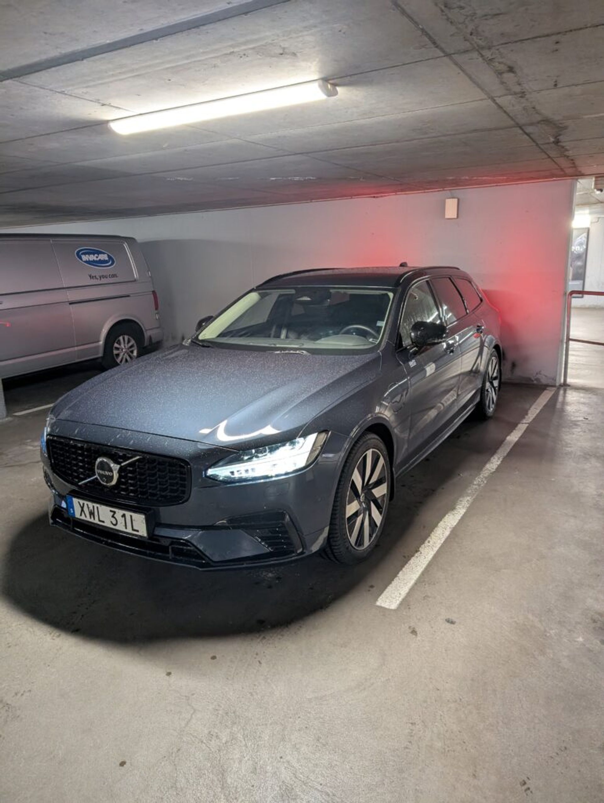 A navy blue Volvo V60 station wagon in a parking garage in Sweden with the lights on.