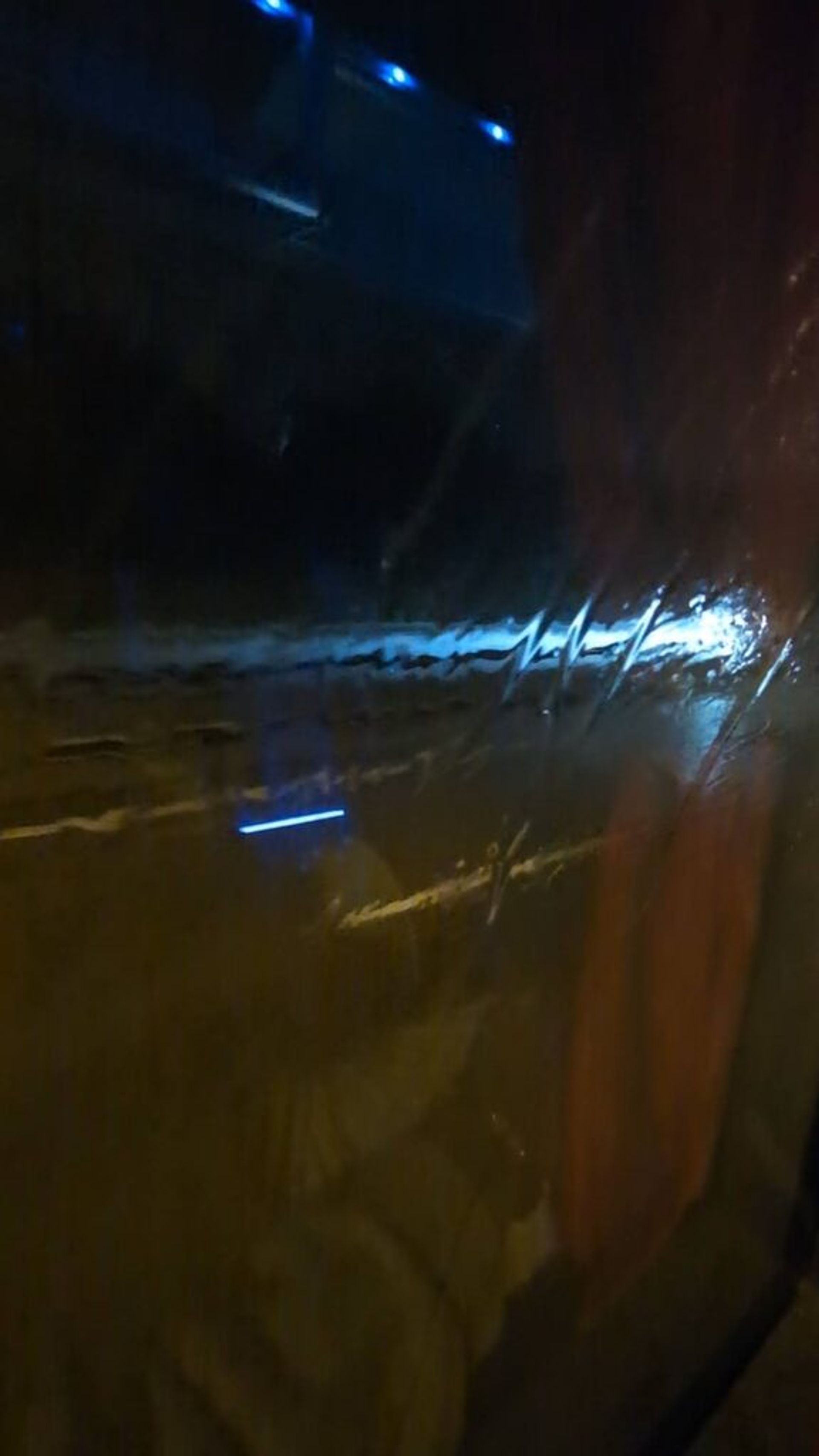 A picture through a bus window covered with water from the rain at night. Outside the window you can see headlights from cars and the markings on the roadway.